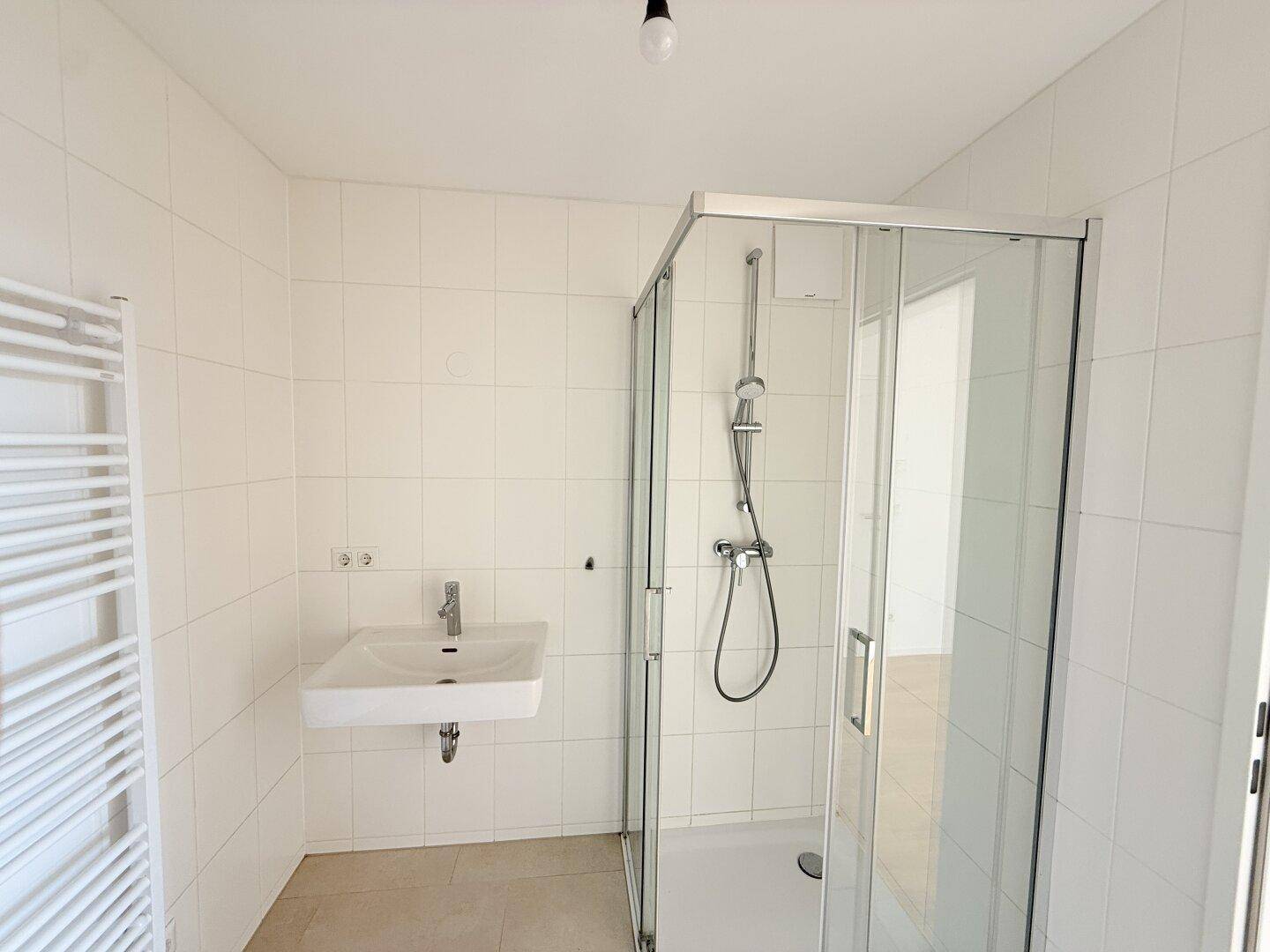 Helles Badezimmer mit Duschkabine, Waschbecken und weißen Wandfliesen.
