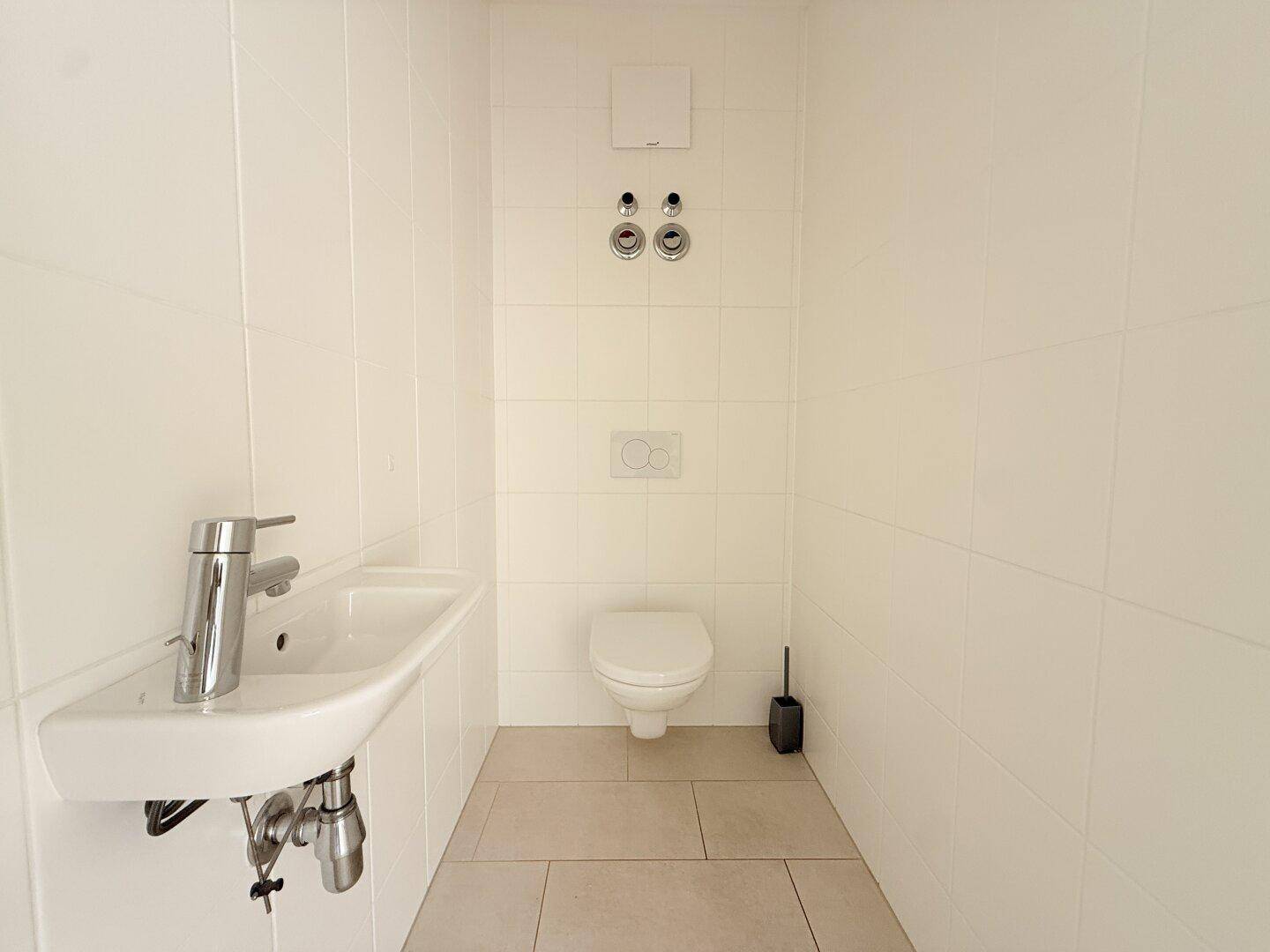Separates WC mit Waschbecken, Toilette und Anschlussmöglichkeiten für eine Waschmaschine.