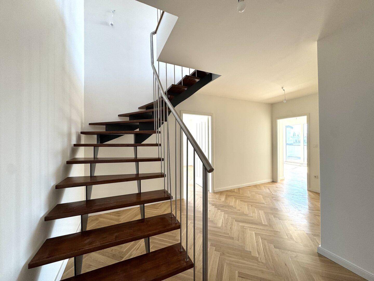 Moderne Holztreppe mit Metallgeländer und Fischgrätparkettboden, verbindet die Wohnebenen stilvoll.