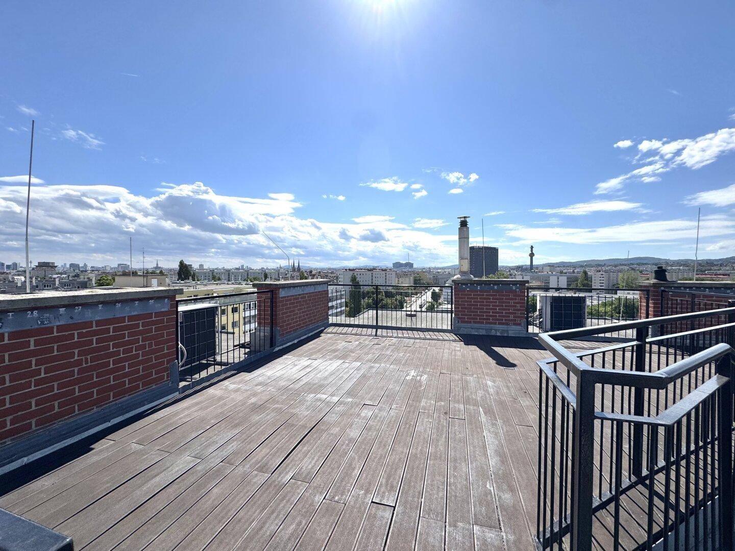 Sonnige Dachterrasse mit Holzdielen und weitem Blick über die Dächer der Stadt und die Landschaft.