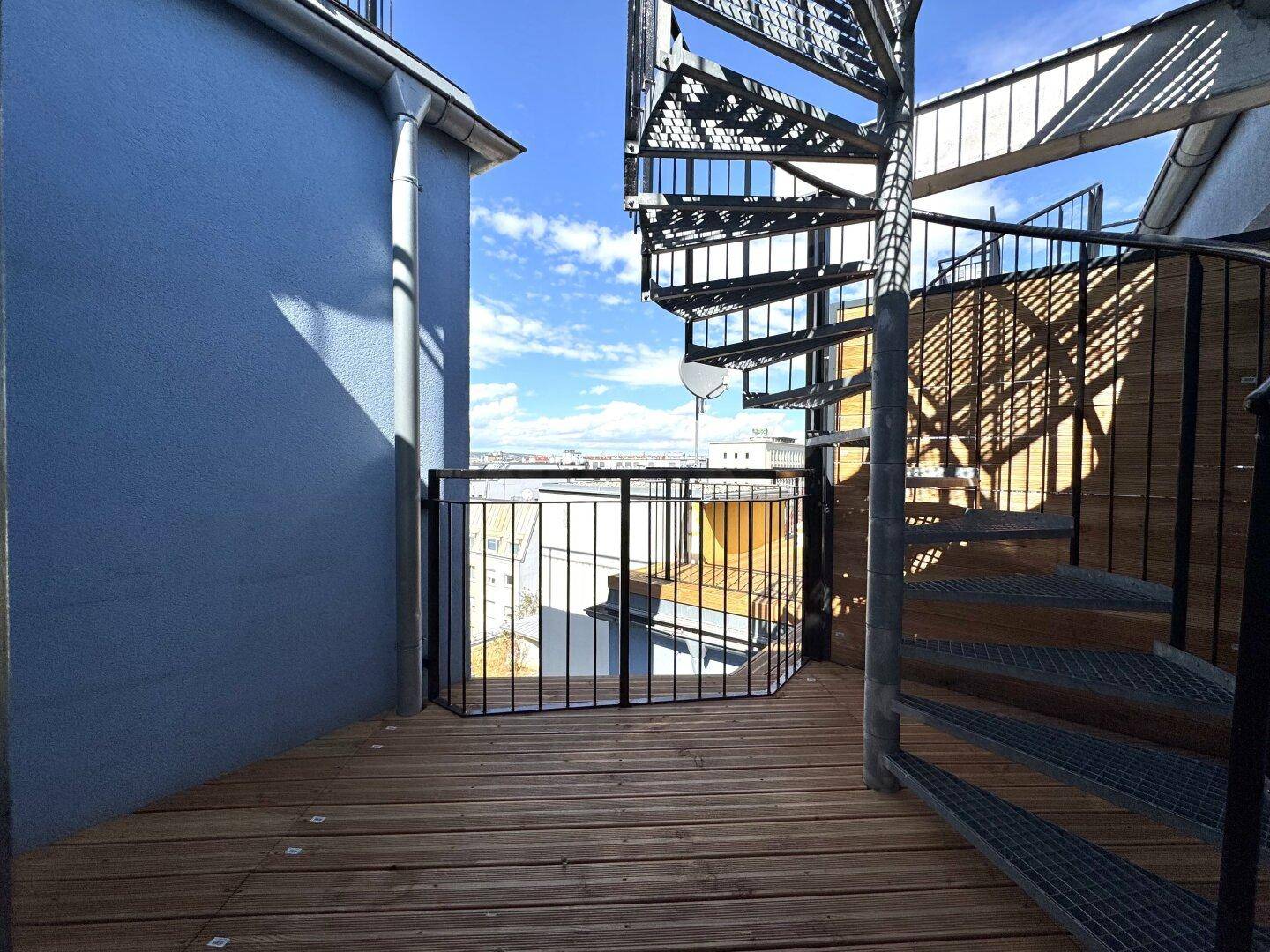 Wendeltreppe aus Metall führt zu einer weiteren Ebene der Dachterrasse mit Holzboden und Stadtblick.