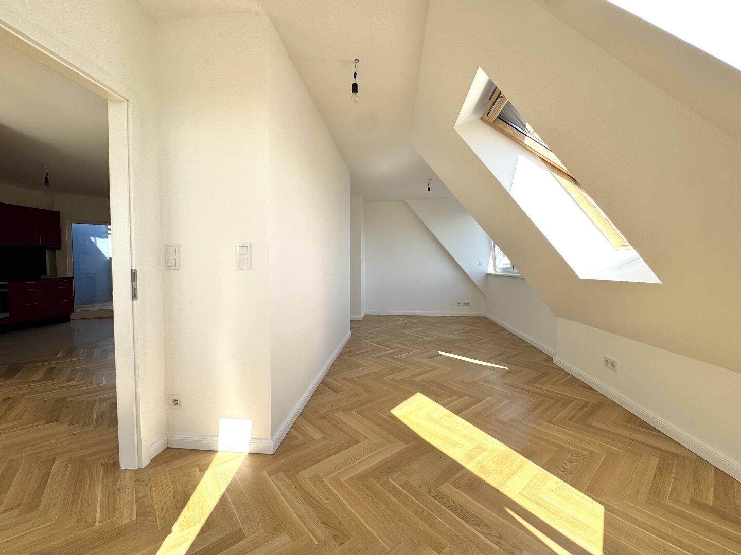 Heller Raum mit Fischgrätparkett, Dachschrägen und einem Dachfenster, bietet viel Tageslicht.