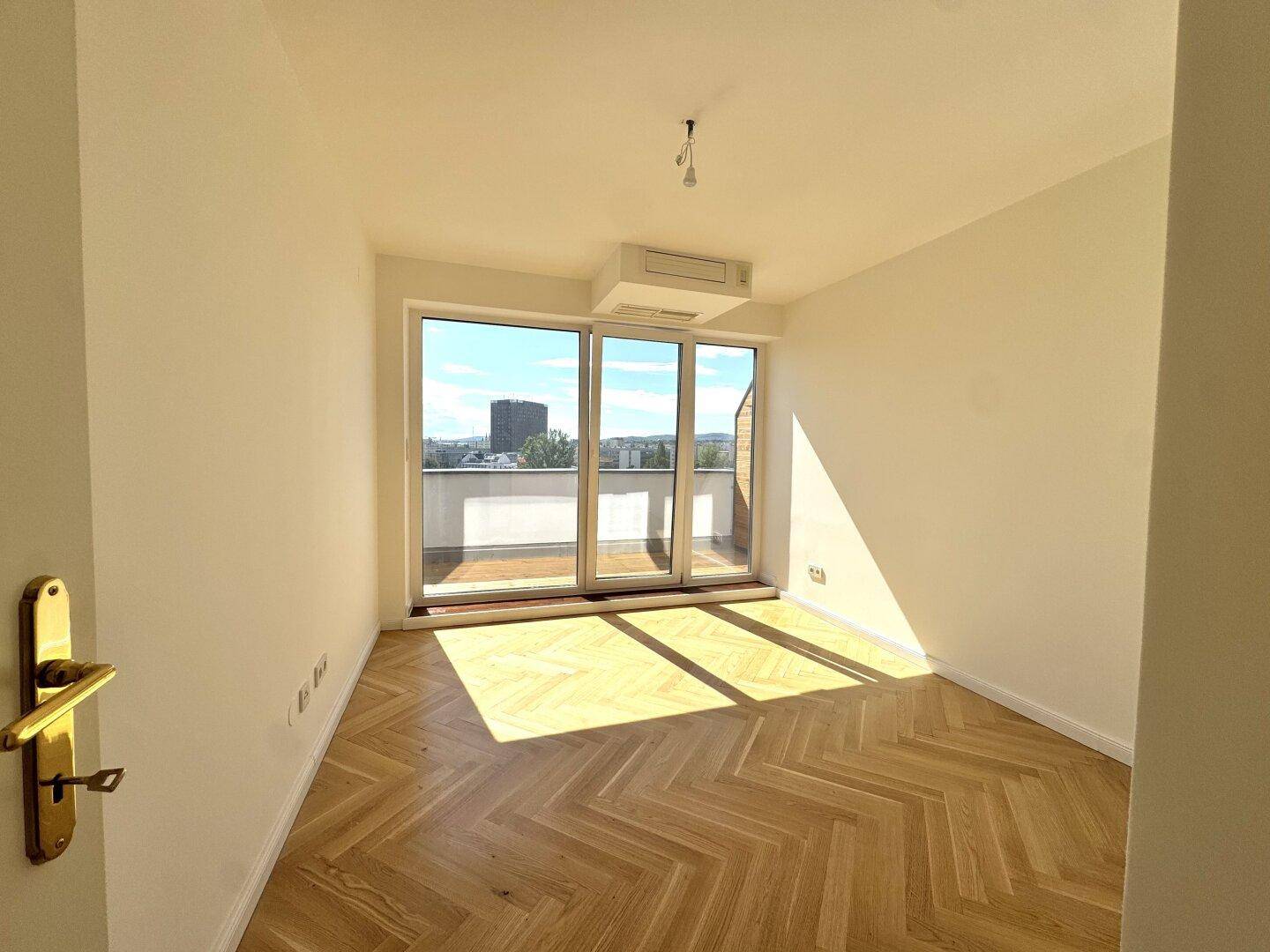 Sonniges Schlafzimmer mit Fischgrätparkett, großen Fenstern und direktem Zugang zum Außenbereich.