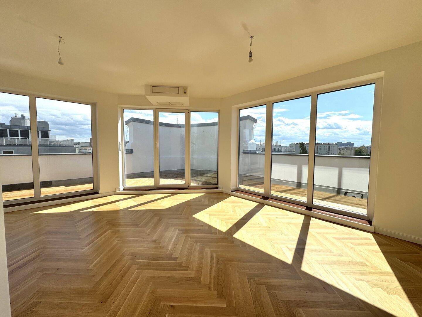 Heller Wohnraum mit Fischgrätparkett, großen Fensterfronten und Zugang zu einer Terrasse.