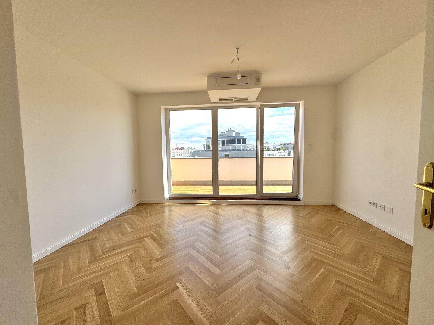 Schlafzimmer mit Fischgrätparkett, großen Fenstern und Zugang zu einem Balkon oder einer Terrasse.