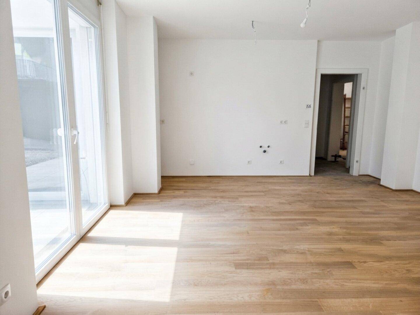 Lichtdurchfluteter Wohnbereich mit hellem Holzboden, weißen Wänden und Terrassenzugang.