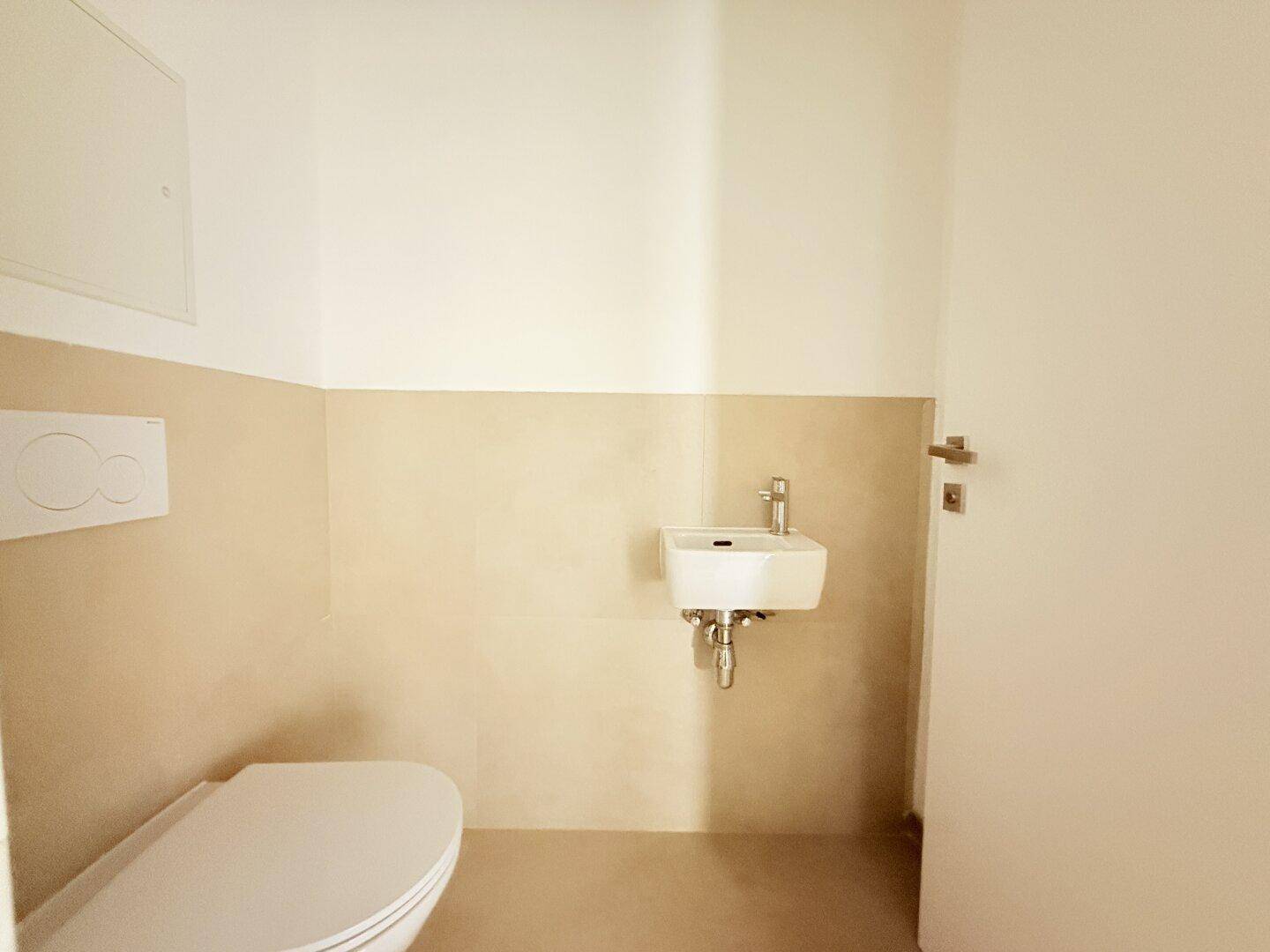 Modernes Gäste-WC mit Wand-WC, kleinem Waschbecken und beigefarbenen Fliesen.