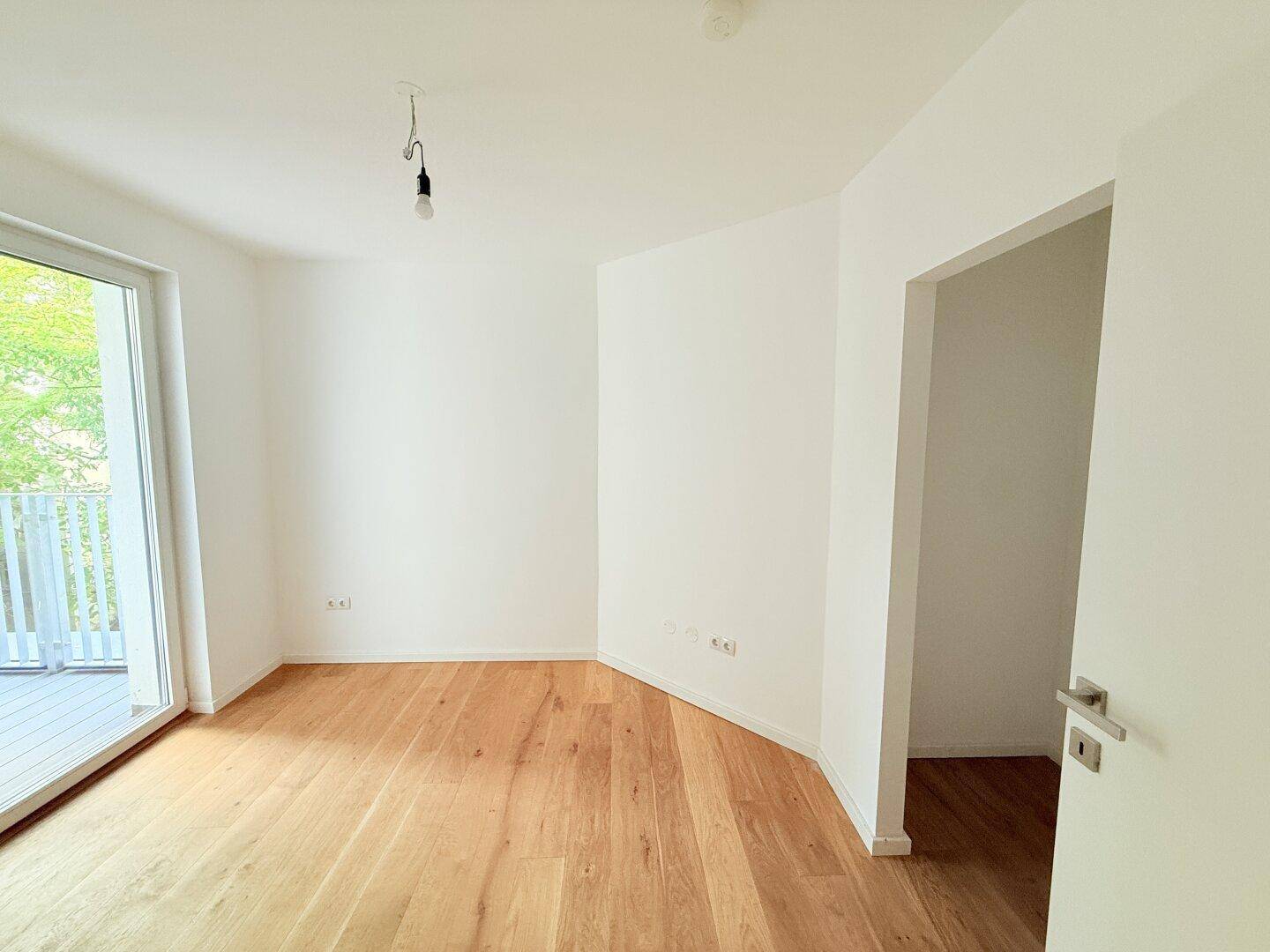 Helles Schlafzimmer mit Holzboden und Zugang zu einem Balkon.