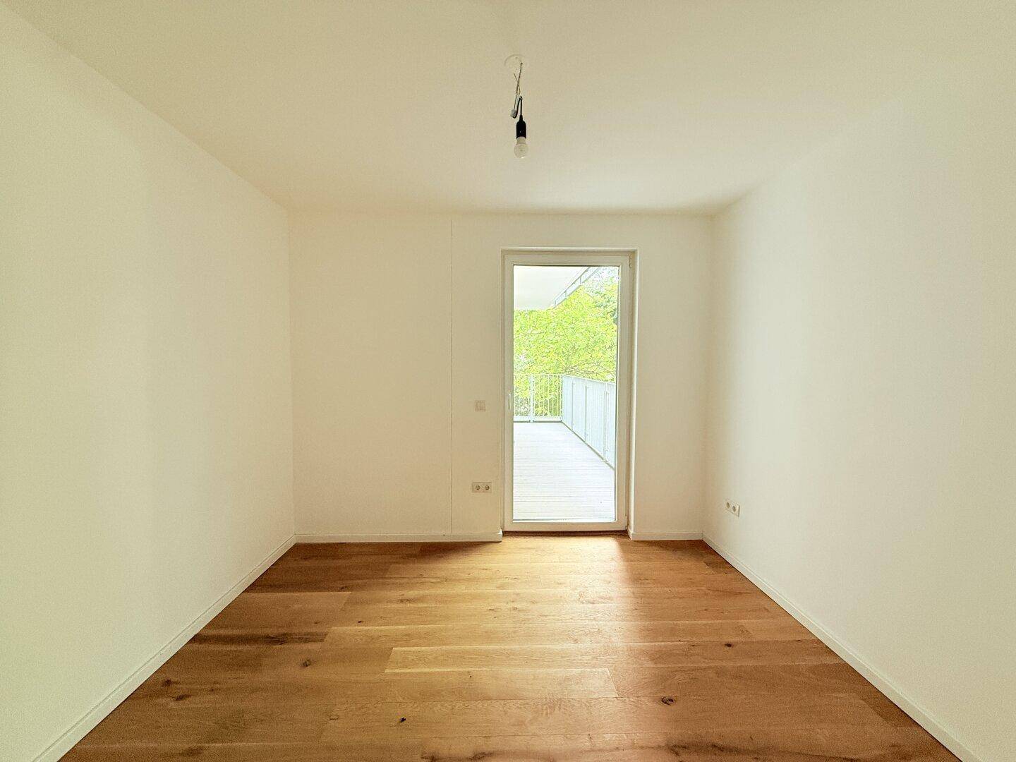 Helles Schlafzimmer mit Holzboden und Balkonzugang, ideal für natürliche Belichtung.