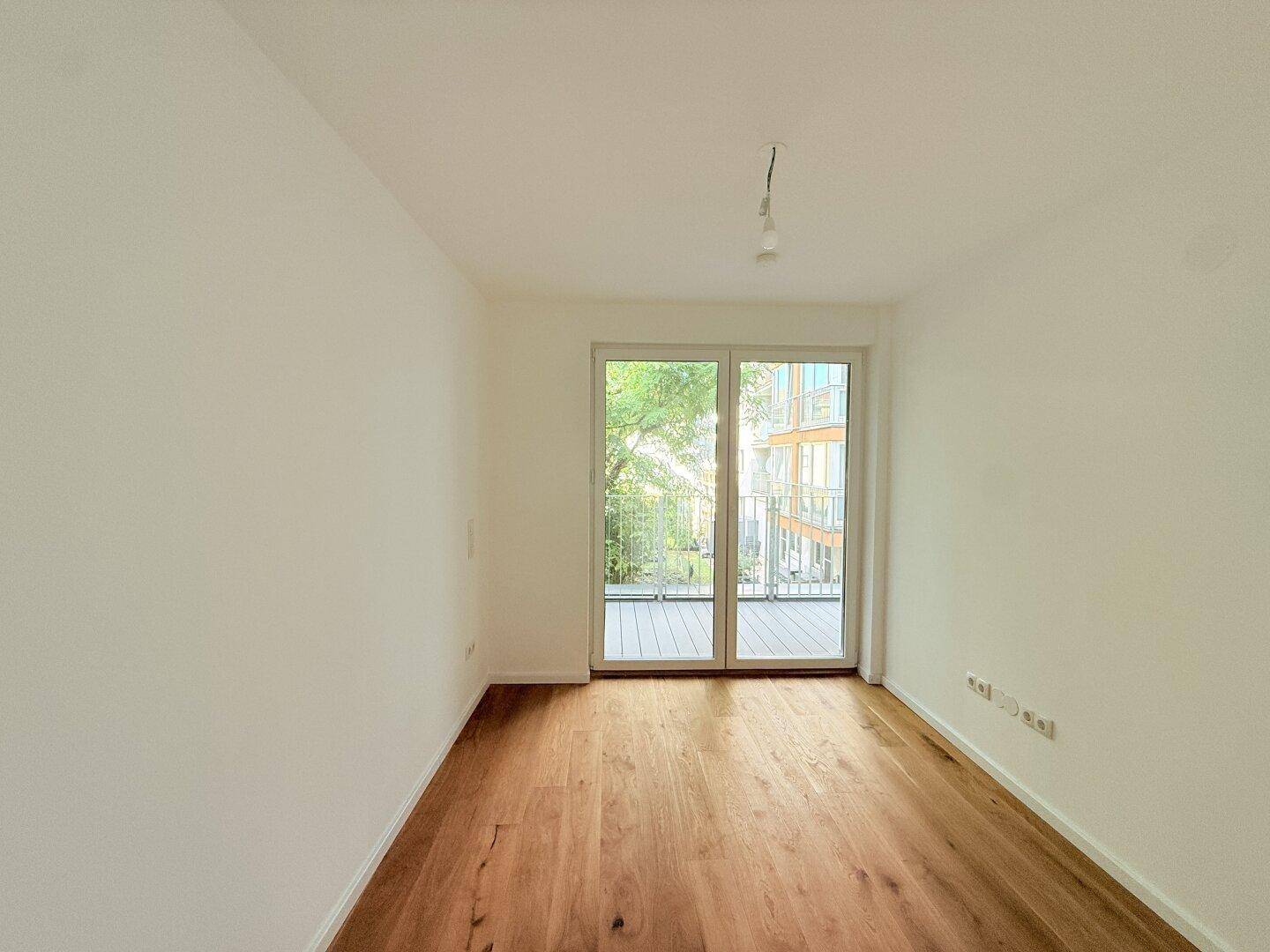 Helles Schlafzimmer mit Holzboden und großen Fenstern zum Balkon.