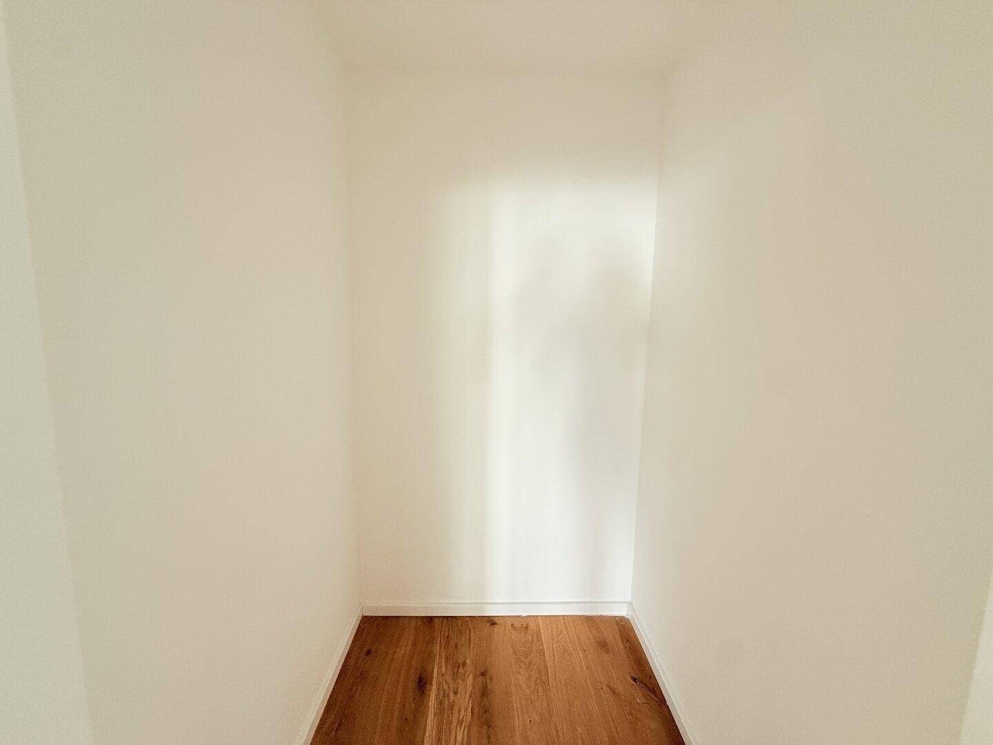 Kleiner, leerer Abstellraum mit Holzboden und weißen Wänden.