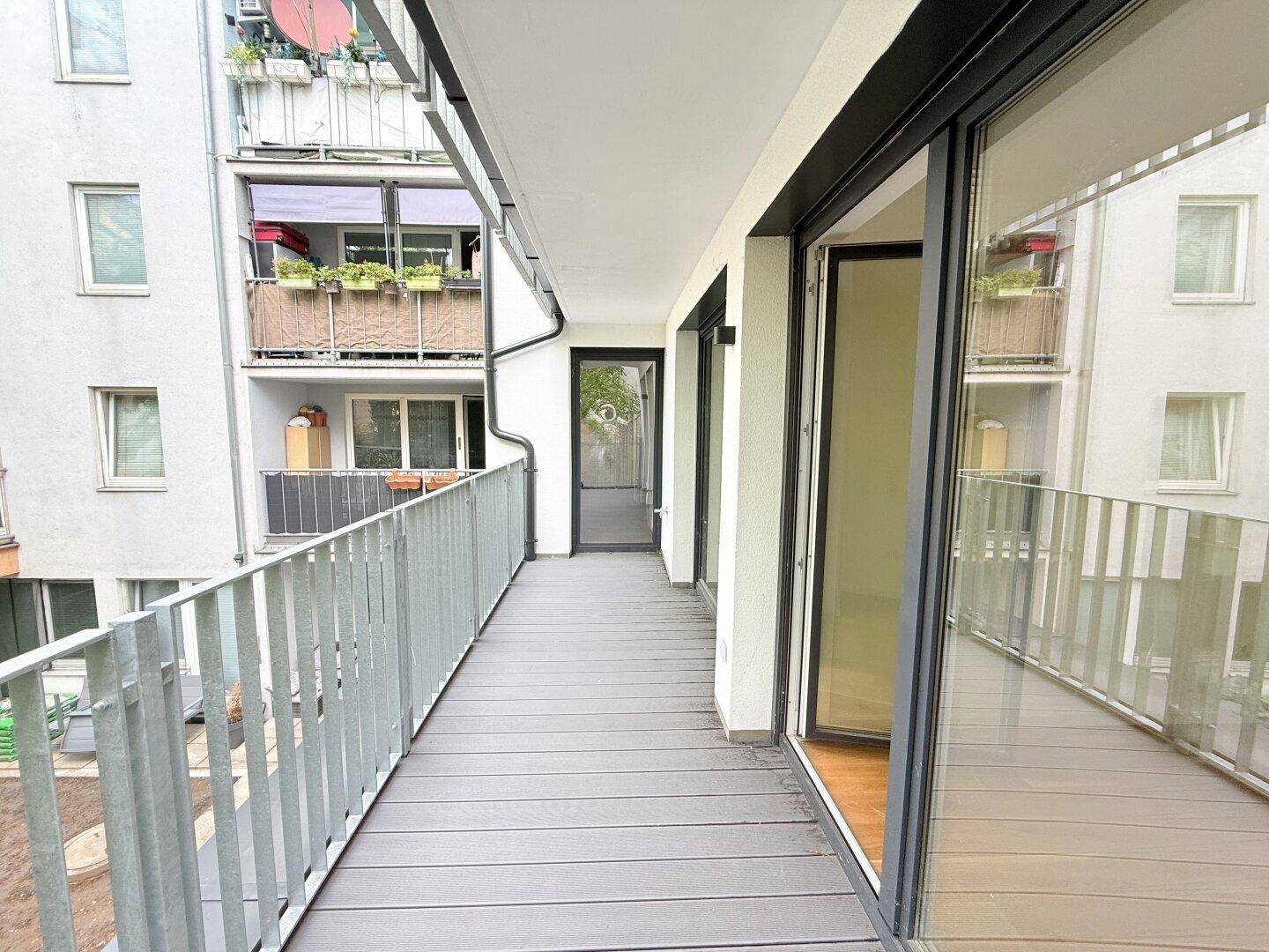 Geräumiger Balkon mit Holzdielen und Blick auf die umliegenden Gebäude.
