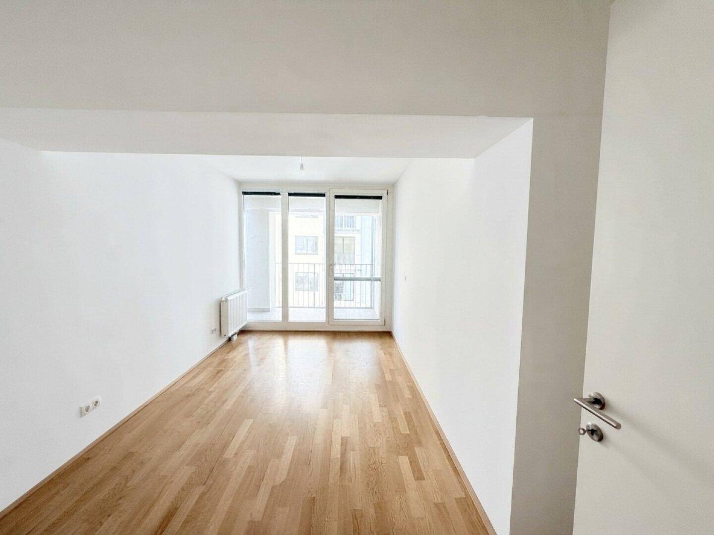 Geräumiges Wohnzimmer mit Parkettboden und großen Fenstern, die viel Tageslicht hereinlassen.