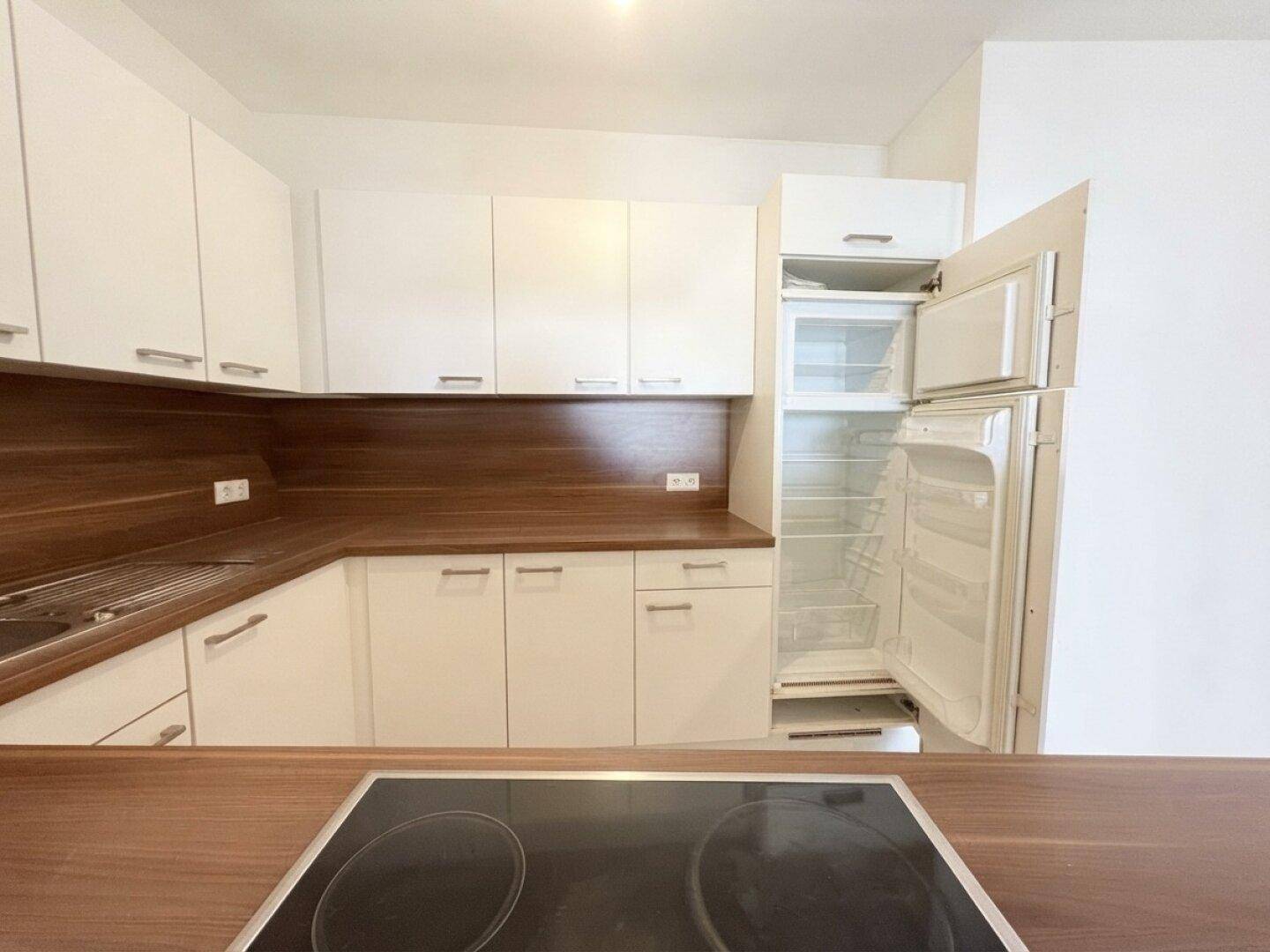 Moderne Küche mit weißen Schränken, Holz-Arbeitsplatten und integriertem Kühlschrank mit Gefrierfach.