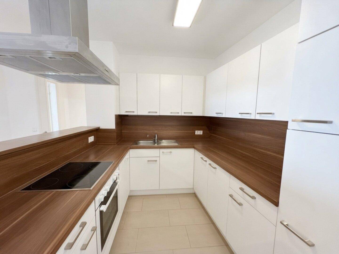 Funktionale Küche mit weißen Schränken, Holz-Arbeitsplatten, Induktionskochfeld und Dunstabzugshaube.
