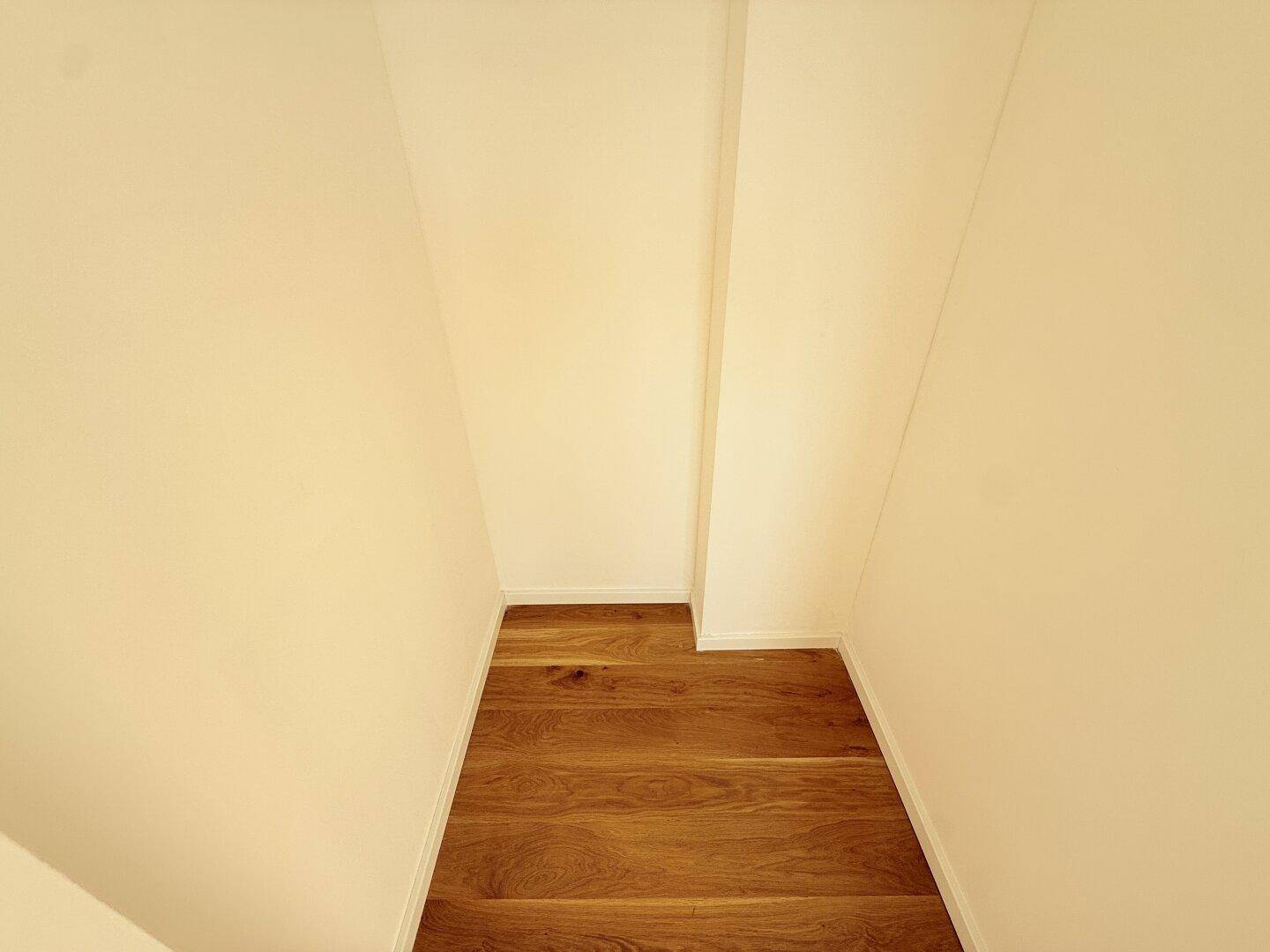 Kleiner Abstellraum mit Holzboden und weißen Wänden, bietet zusätzlichen Stauraum für Haushaltsgegenstände.