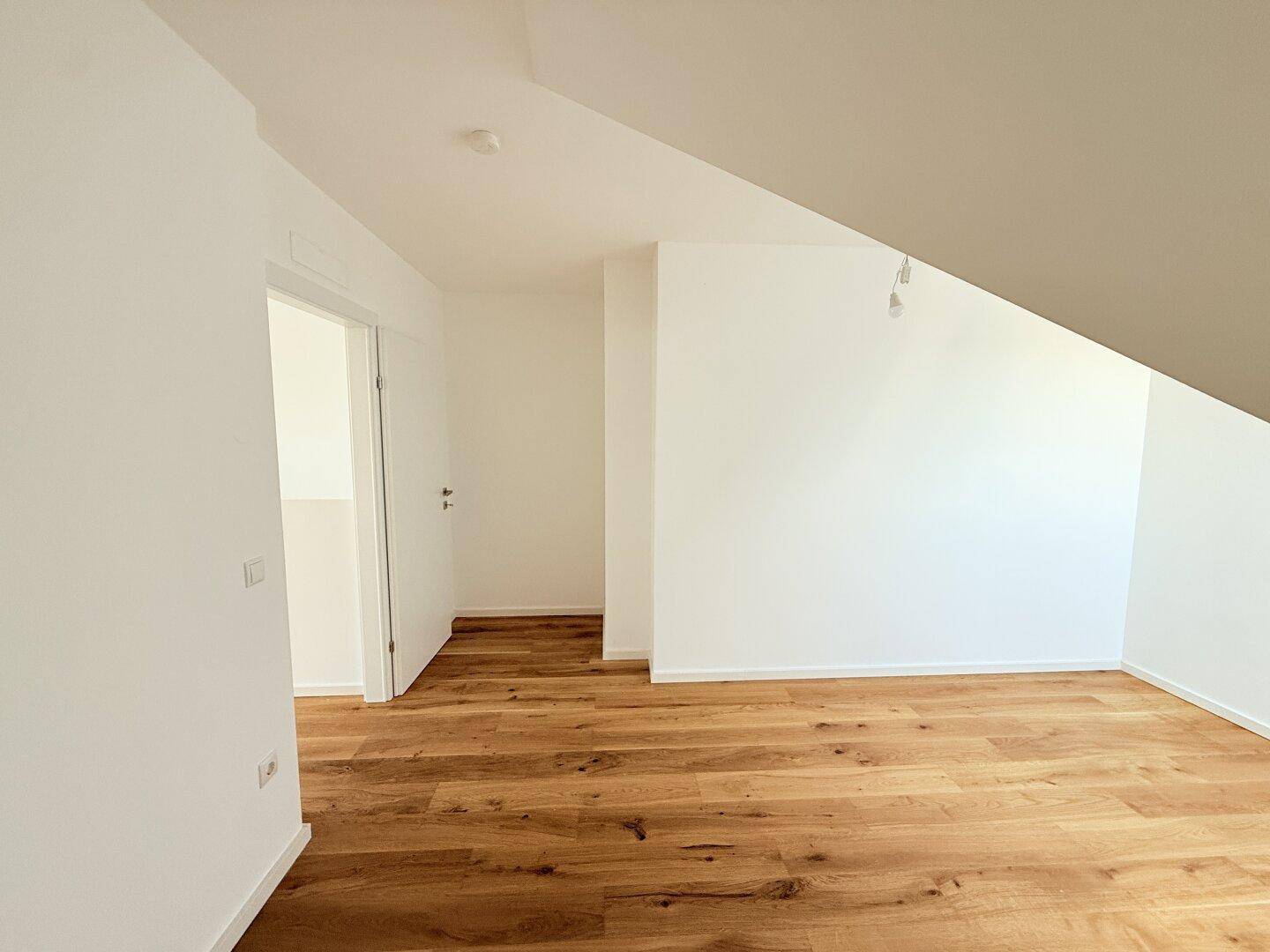 Heller Raum im Dachgeschoss mit Holzboden und Zugang zu weiteren Zimmern.