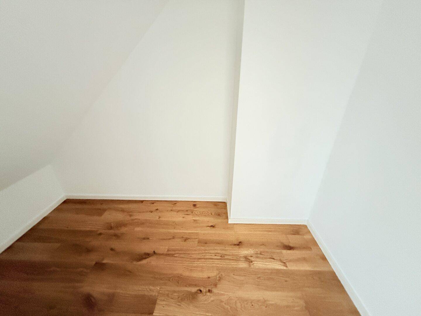 Kleiner, heller Bereich im Dachgeschoss mit Holzboden und schrägen Wänden.