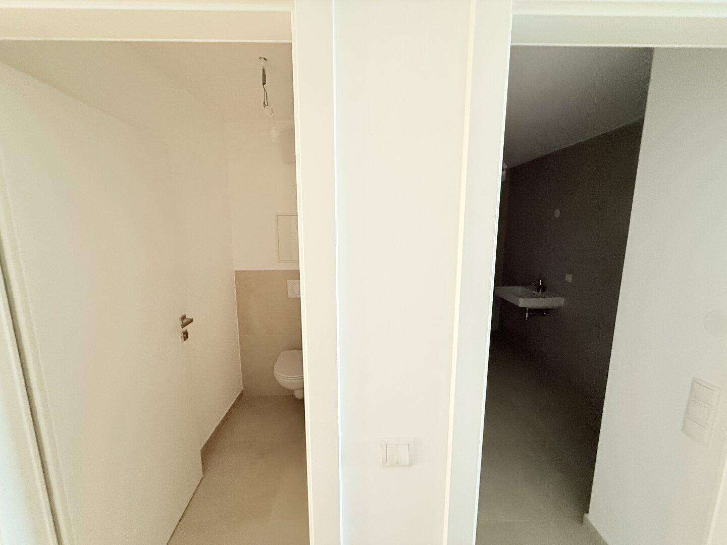 Blick in zwei separate Räume, einer davon ein Gäste-WC mit modernem Design.