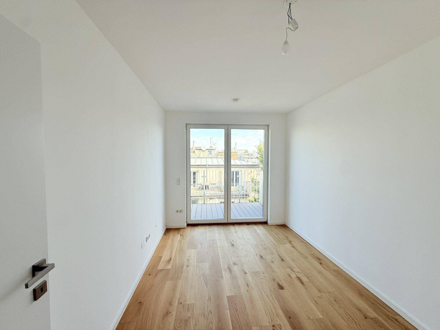 Heller Raum mit Holzboden und Zugang zu einem Balkon, ideal als Schlafzimmer.