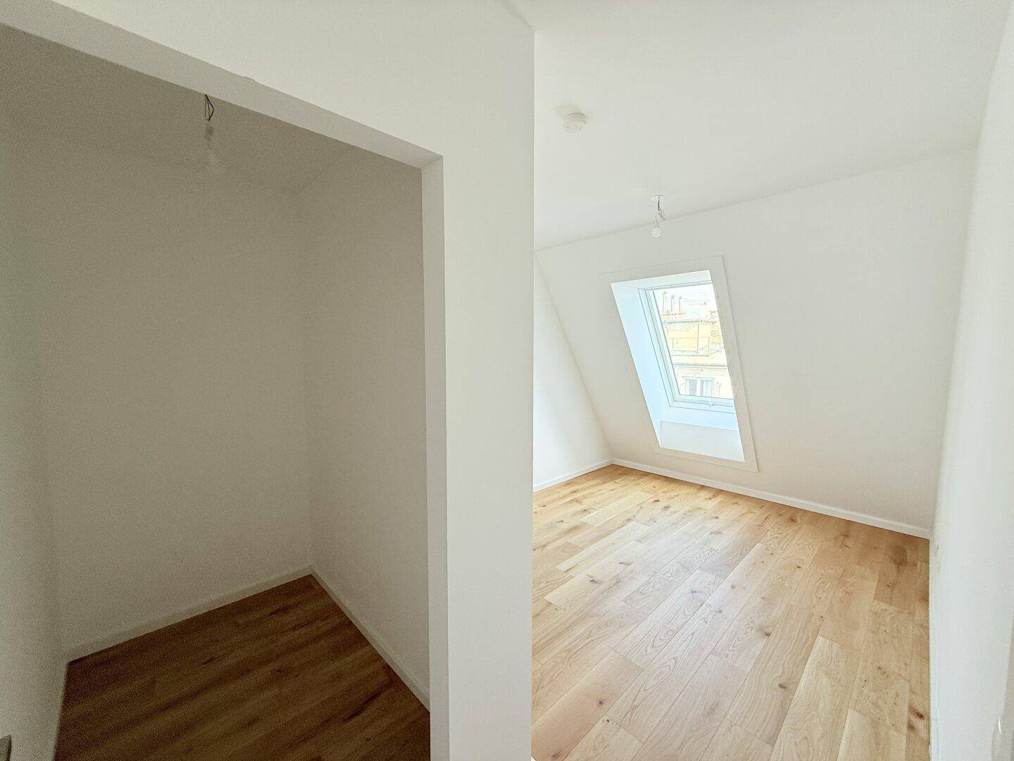 Heller Raum mit Holzboden und Dachfenster, daneben ein kleiner Abstellbereich.