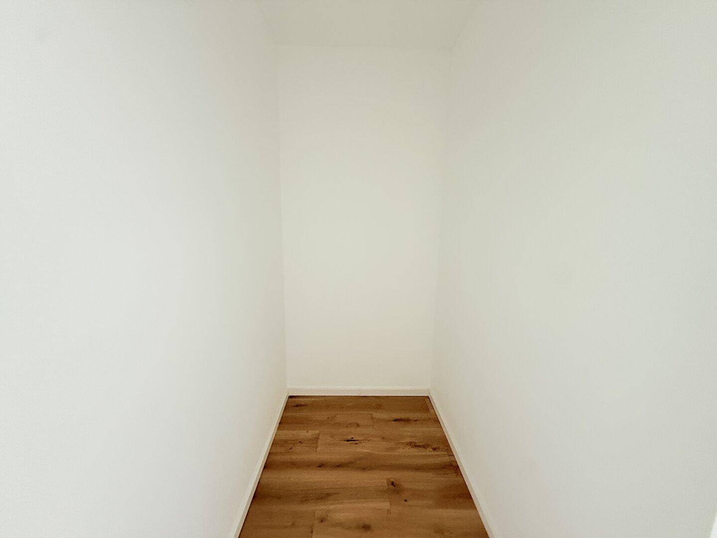 Kleiner, heller Abstellraum mit Holzboden und weiß gestrichenen Wänden.