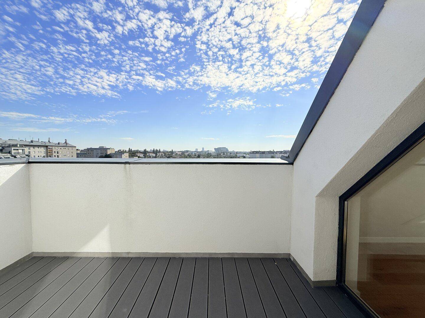 Geräumiger Balkon mit modernem Bodenbelag und weitem Blick über die Stadt unter blauem Himmel.