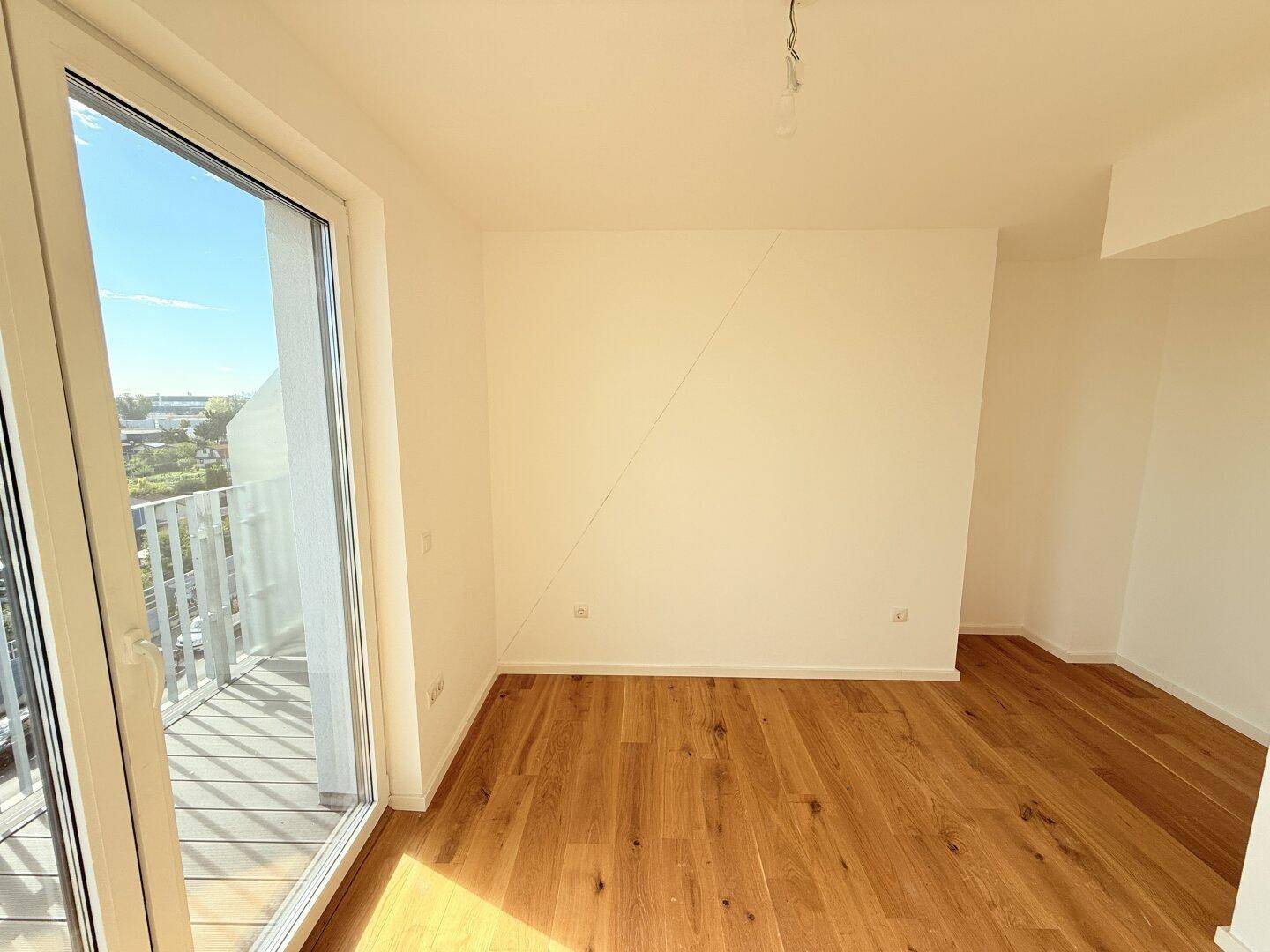 Geräumiges Schlafzimmer mit Holzboden und viel Tageslicht durch die große Balkontür.