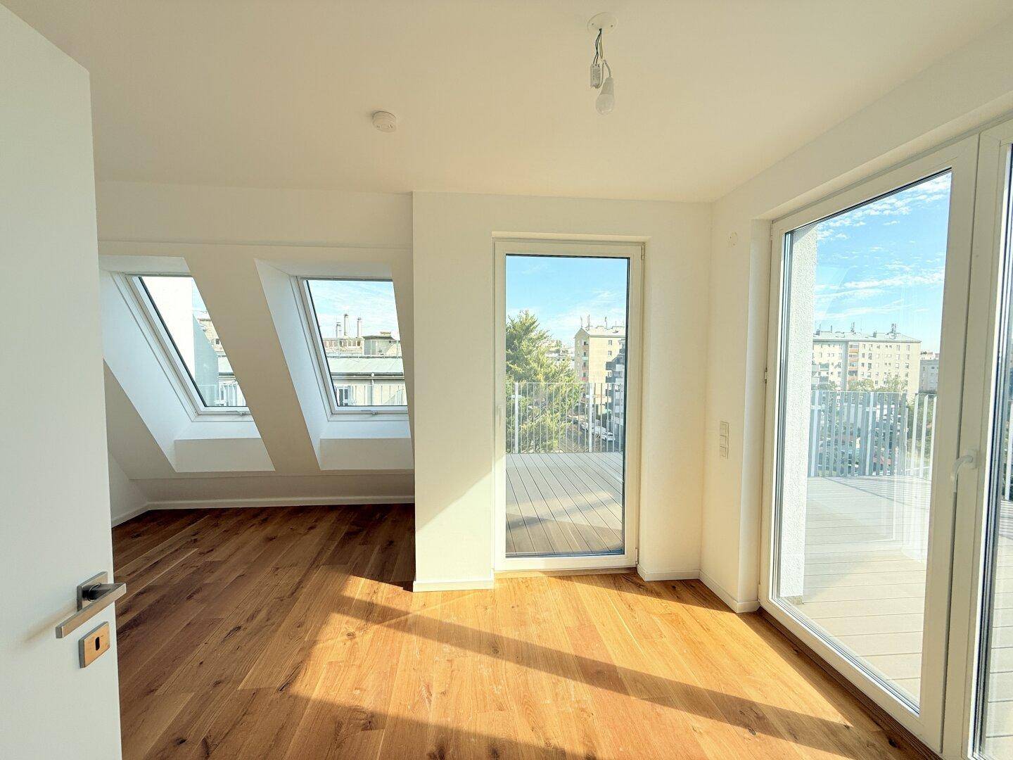 Heller Wohnbereich mit Holzboden, Zugang zum Balkon und Blick auf weitere Dachfensterbereiche.