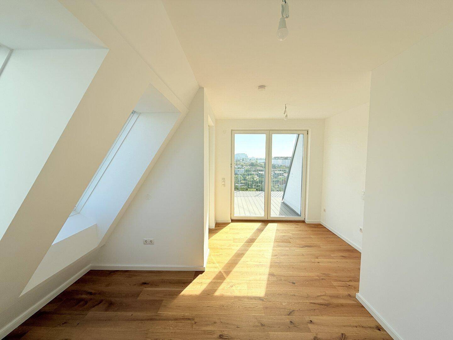 Geräumiges Dachgeschosszimmer mit Holzboden, Zugang zum Balkon und einem weiteren Dachfenster.