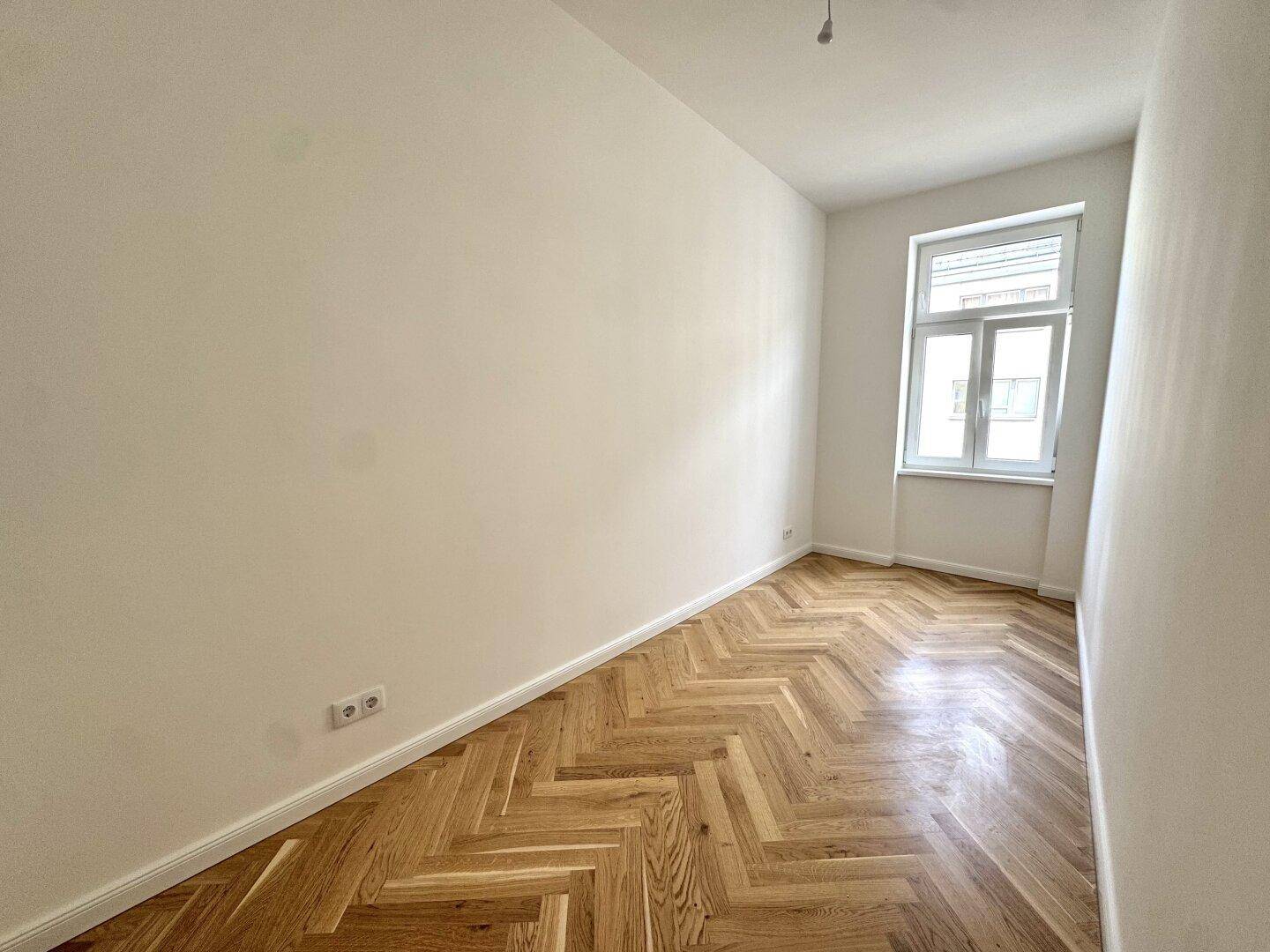 Gemütliches Zimmer mit Fischgrätparkett und einem großen Fenster, bietet viel natürliches Licht.