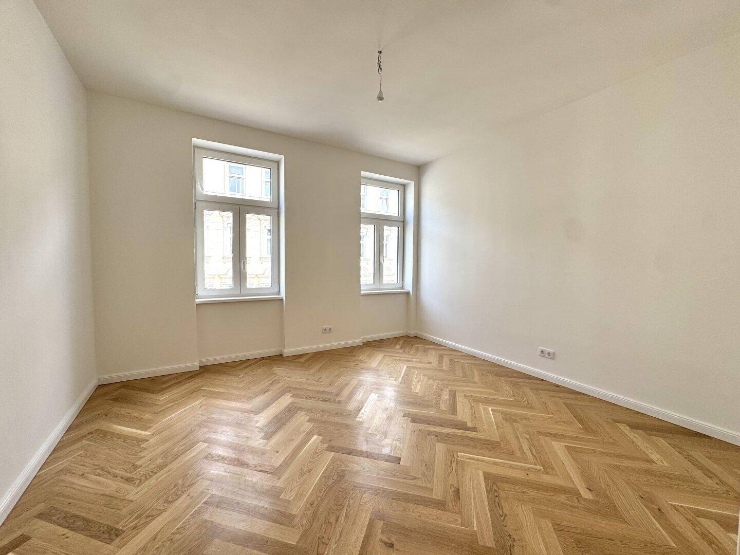 Ruhiges Zimmer mit zwei Fenstern und elegantem Fischgrätparkett, ideal als Schlaf- oder Arbeitszimmer.