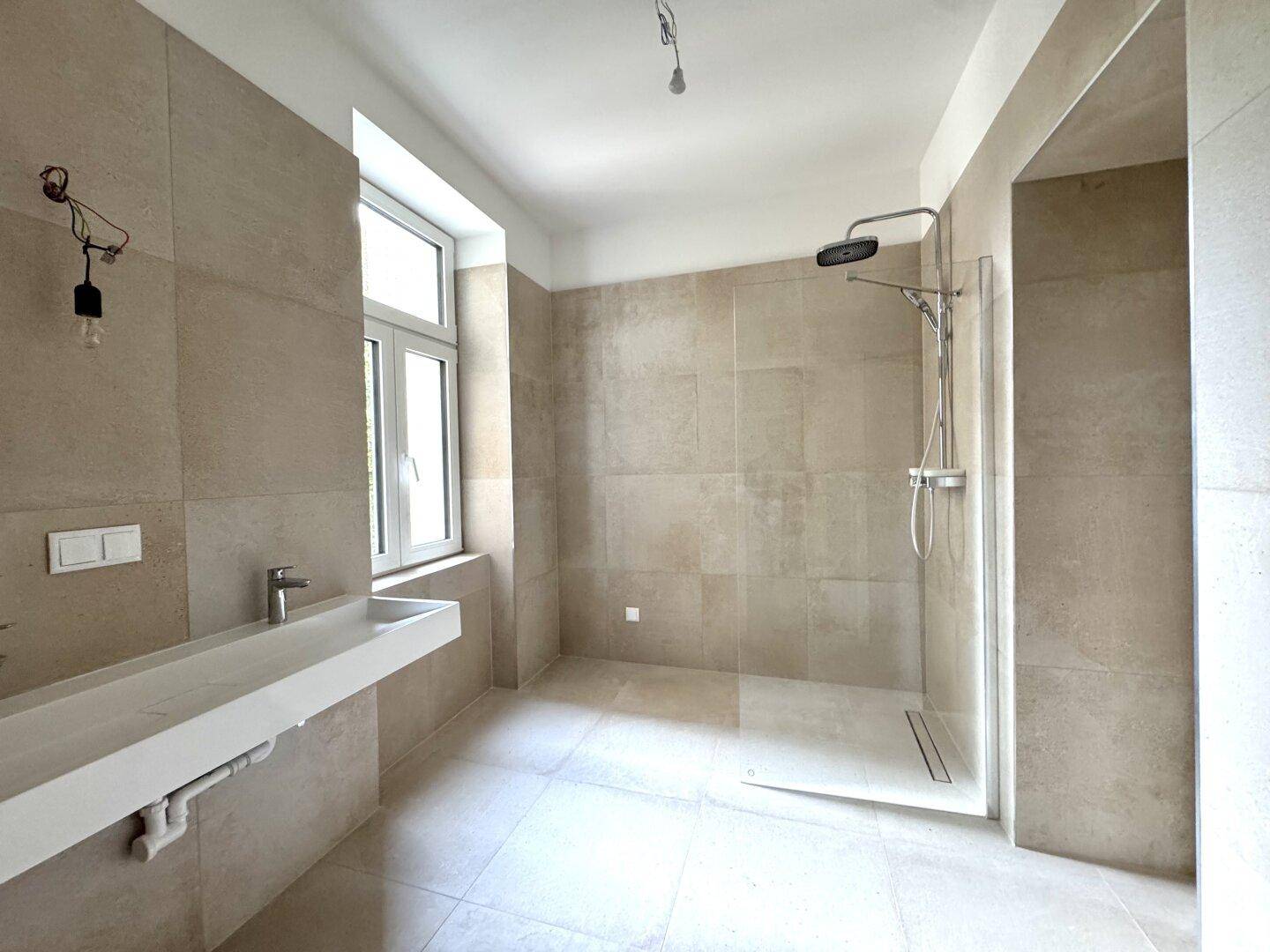 Modernes Badezimmer mit großformatigen Fliesen, ebenerdiger Dusche und breitem Waschbecken.