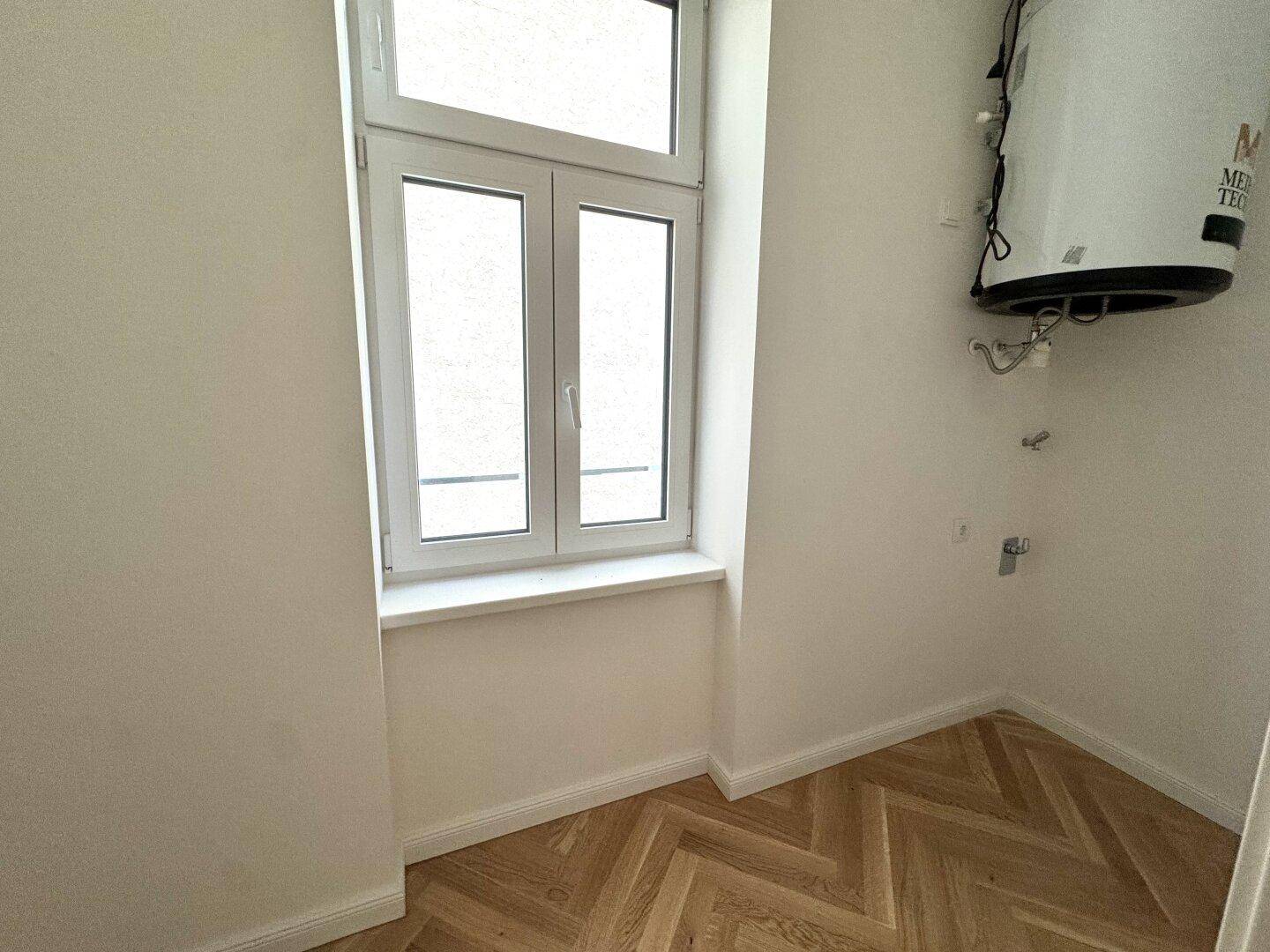 Kleiner Raum mit Fenster und Warmwasserboiler, ideal als Abstell- oder Hauswirtschaftsraum.