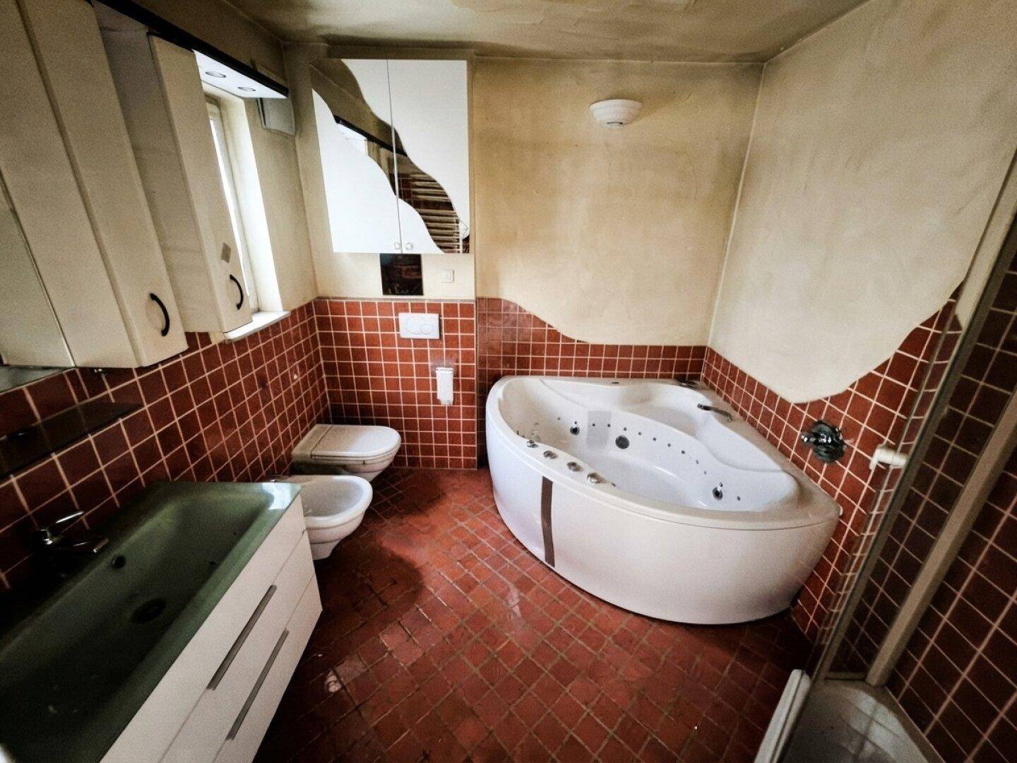 Badezimmer mit Eck-Whirlpool, Bidet, WC und roten Fliesen im Retro-Stil.