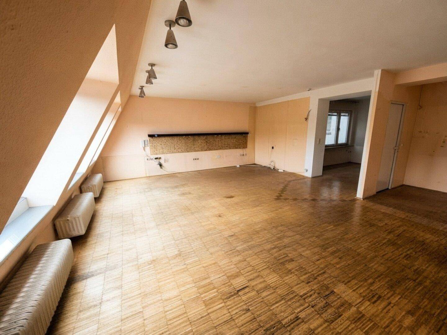 Großer Dachgeschossraum mit schrägen Wänden, Holzparkett und viel natürlichem Licht.