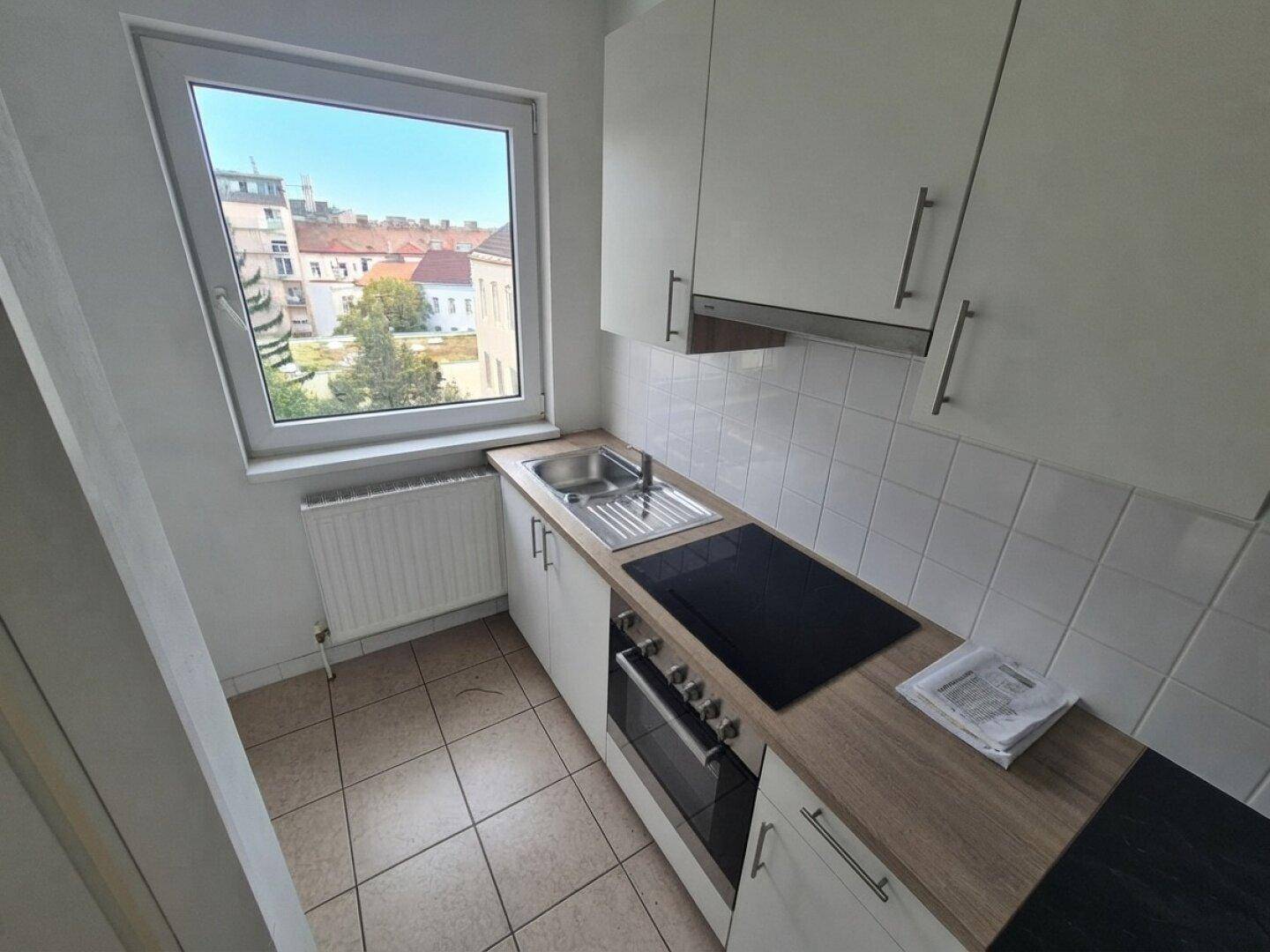 Kleine, funktionale Küche mit weißen Schränken, Holz-Arbeitsplatte und Fenster mit Stadtblick.