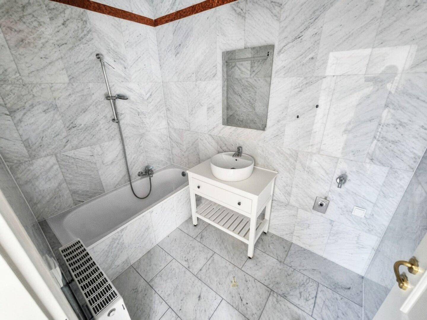 Modernes Badezimmer mit eleganten Marmorfliesen, Badewanne mit Duschfunktion und Einzelwaschbecken.