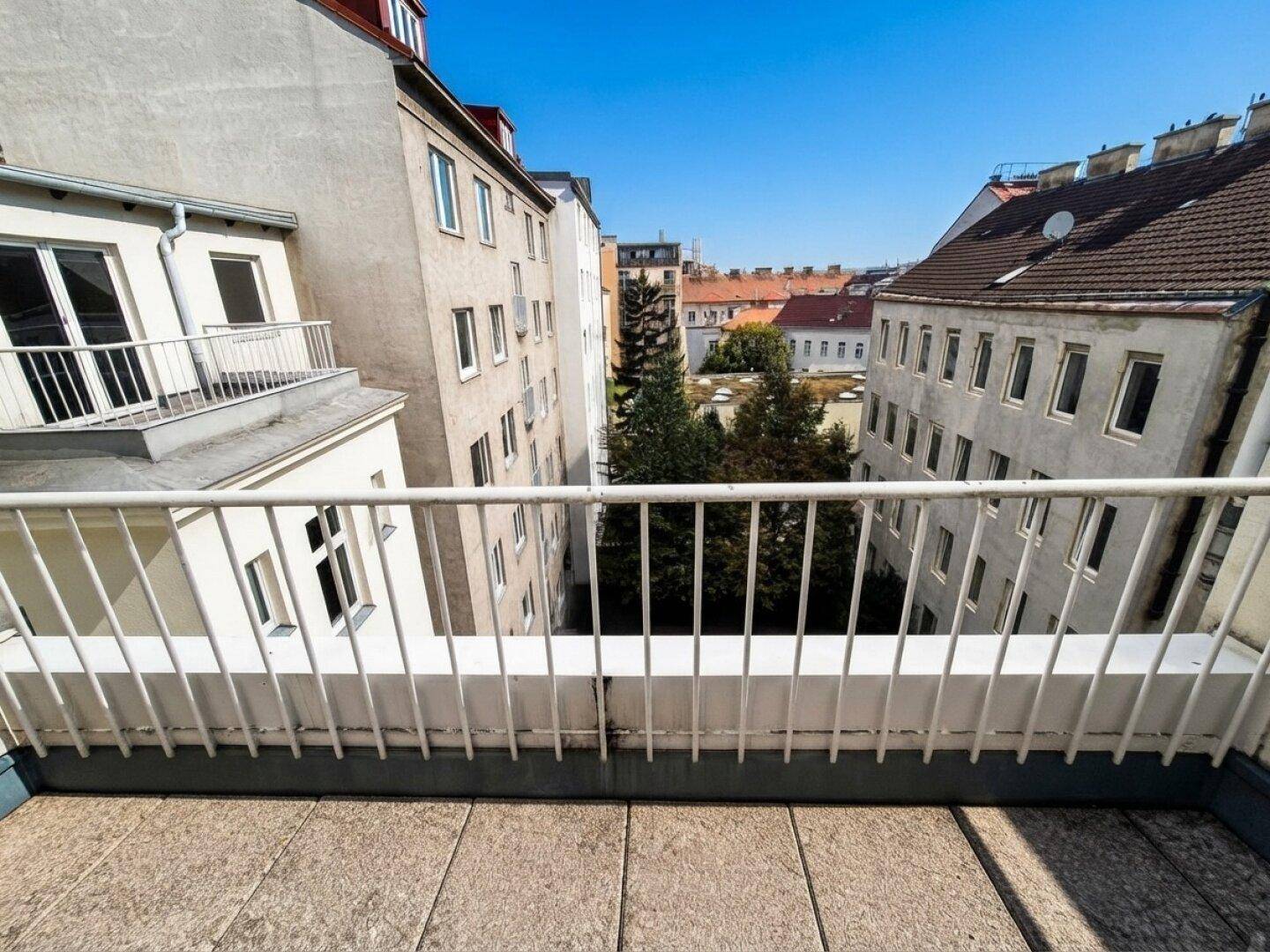 Balkon mit Fliesenboden und weißem Geländer, bietet einen Blick auf den grünen Innenhof.