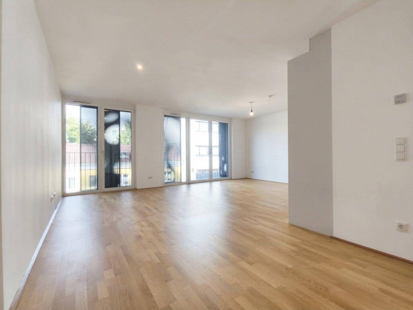 Geräumiges Wohnzimmer mit viel Tageslicht, Parkettboden und moderner, minimalistischer Gestaltung.