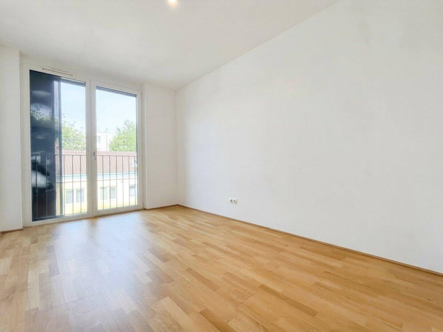 Geräumiges Schlafzimmer mit viel Tageslicht, Parkettboden und Zugang zu einem französischen Balkon.