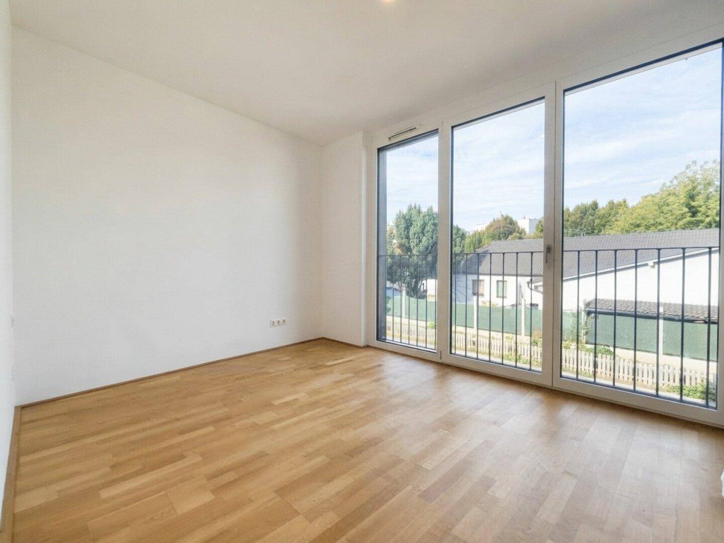 Helles Schlafzimmer mit Parkettboden, großen Fenstern und Blick auf die umliegende Nachbarschaft.