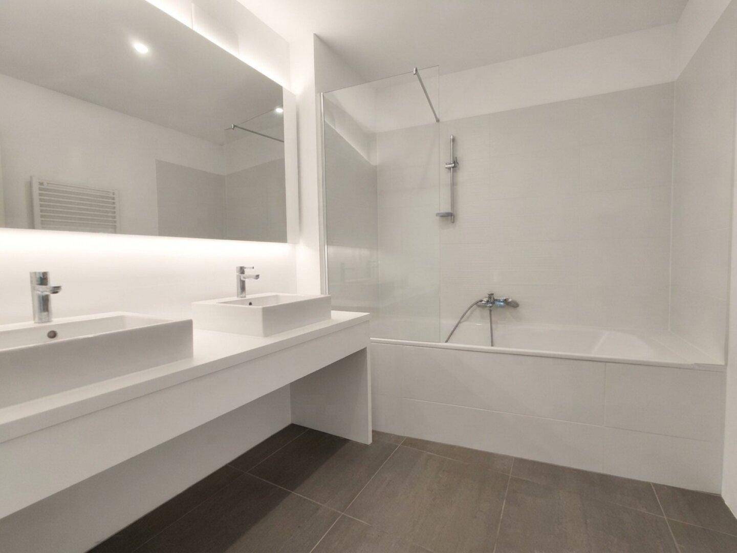 Modernes Badezimmer mit Doppelwaschbecken, Badewanne und eleganten, großen Fliesen.