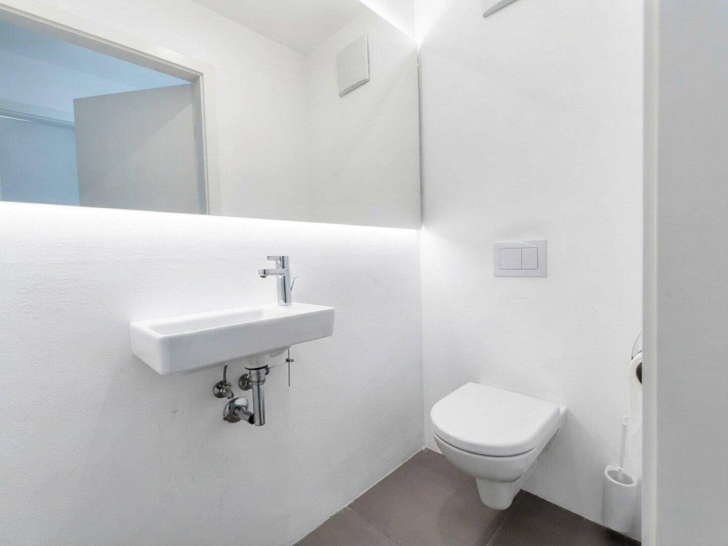 Modernes Gäste-WC mit wandhängender Toilette, kleinem Waschbecken und minimalistischem Design.