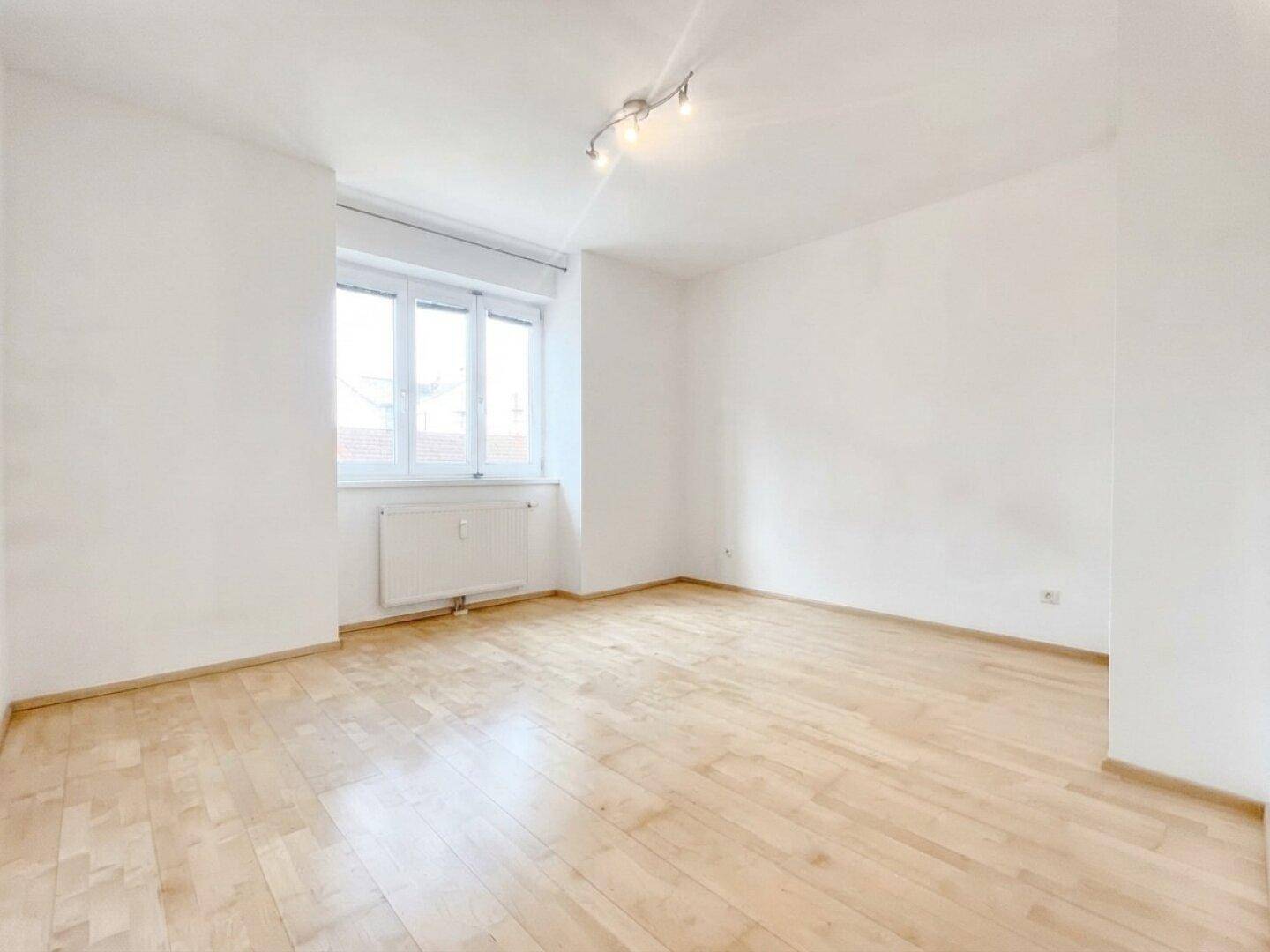 Helles Schlafzimmer mit Parkettboden und großem Fenster.
