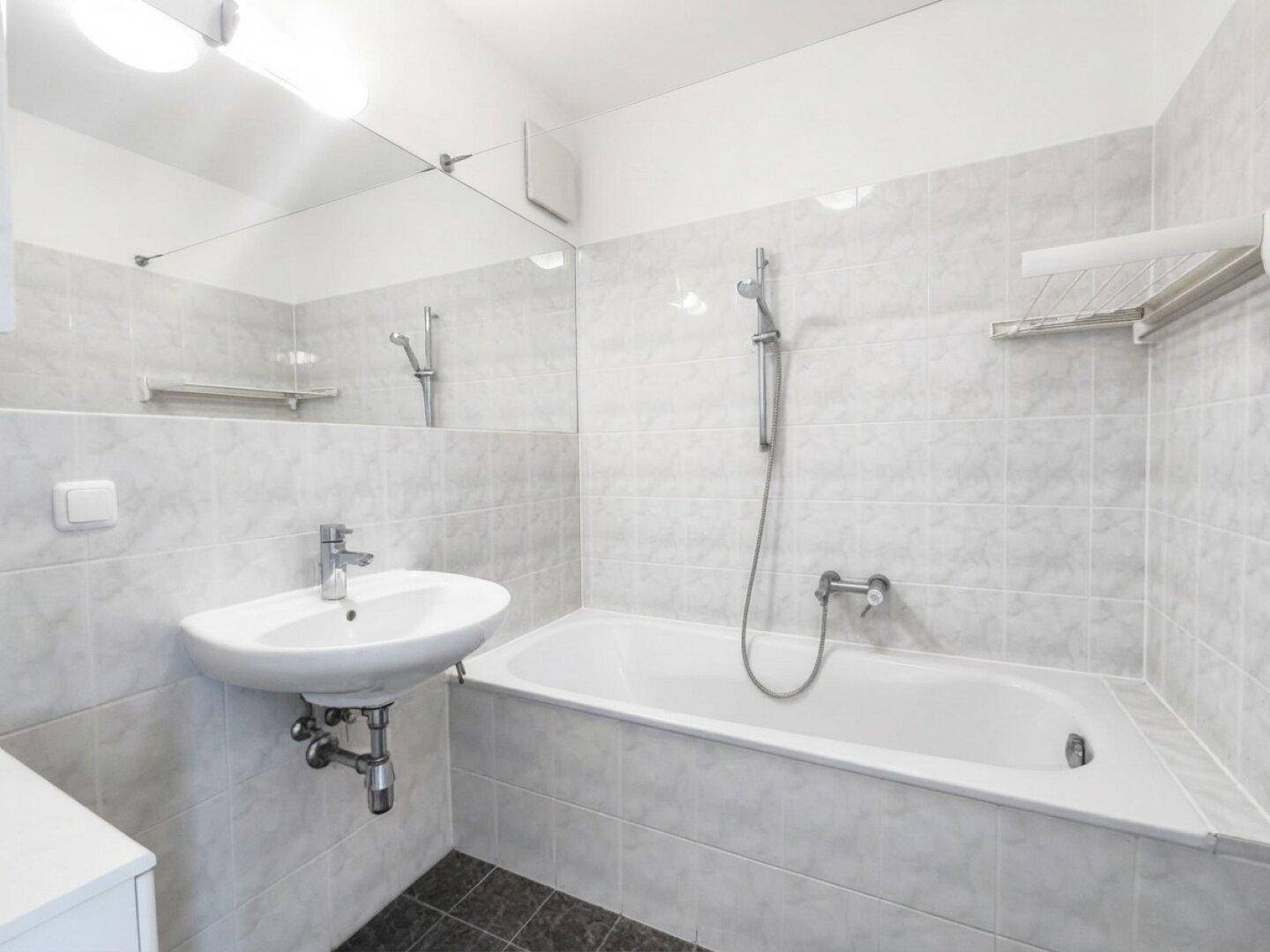 Badezimmer mit Badewanne, Waschbecken und hellgrauen Fliesen.
