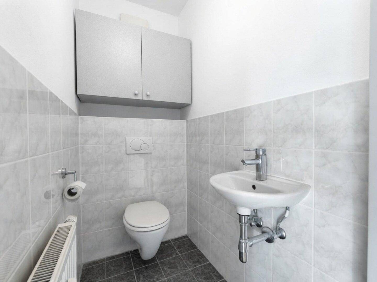 Separates WC mit Toilette, kleinem Waschbecken und Wandfliesen.