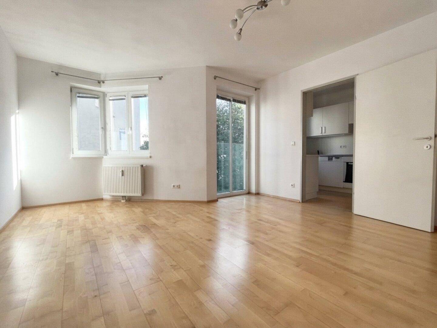 Geräumiges Wohnzimmer mit Holzboden und offenem Zugang zur Küche.