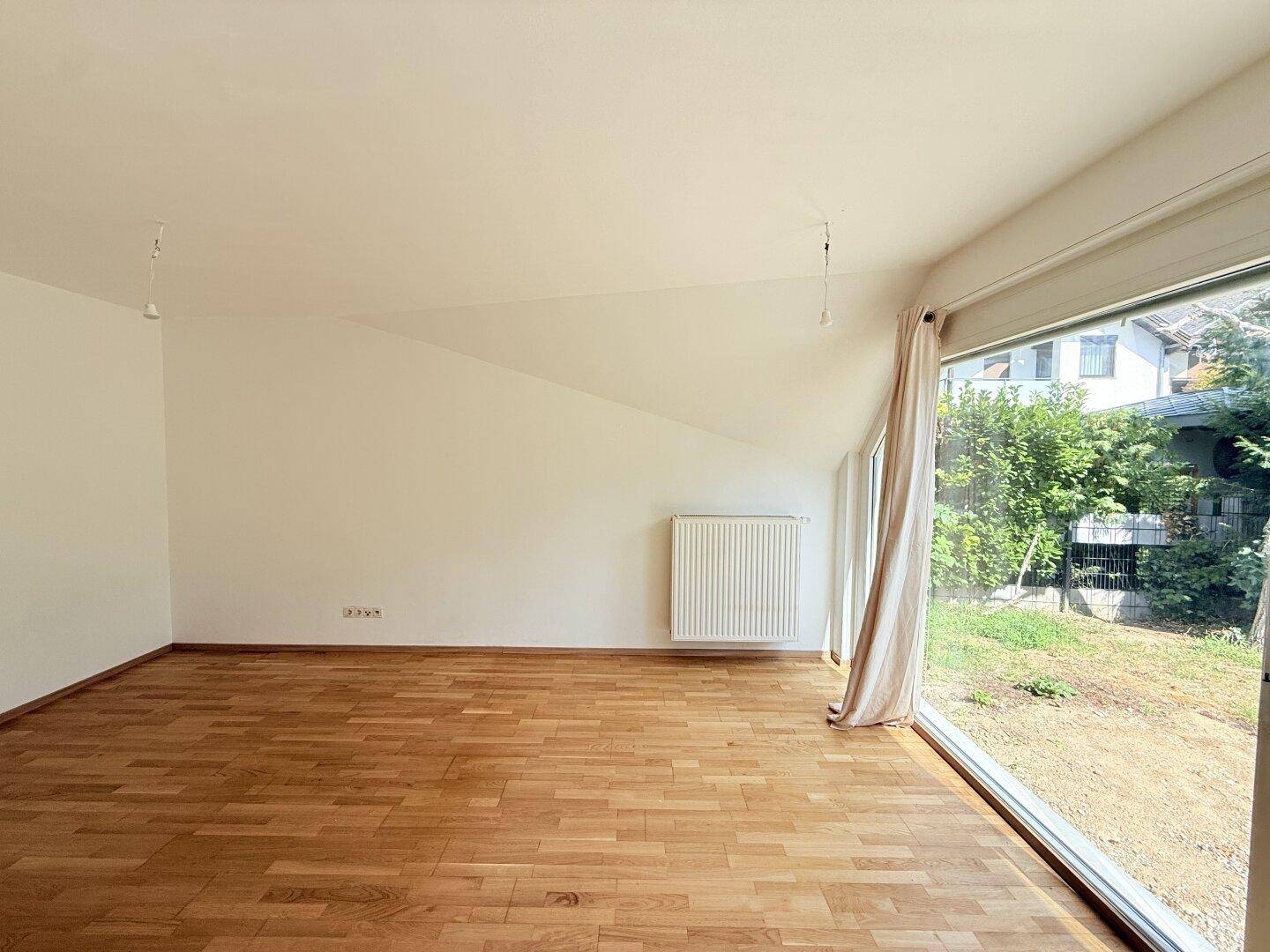 Helles Zimmer mit Holzparkett und großen Fenstern, die einen Blick ins Grüne bieten.