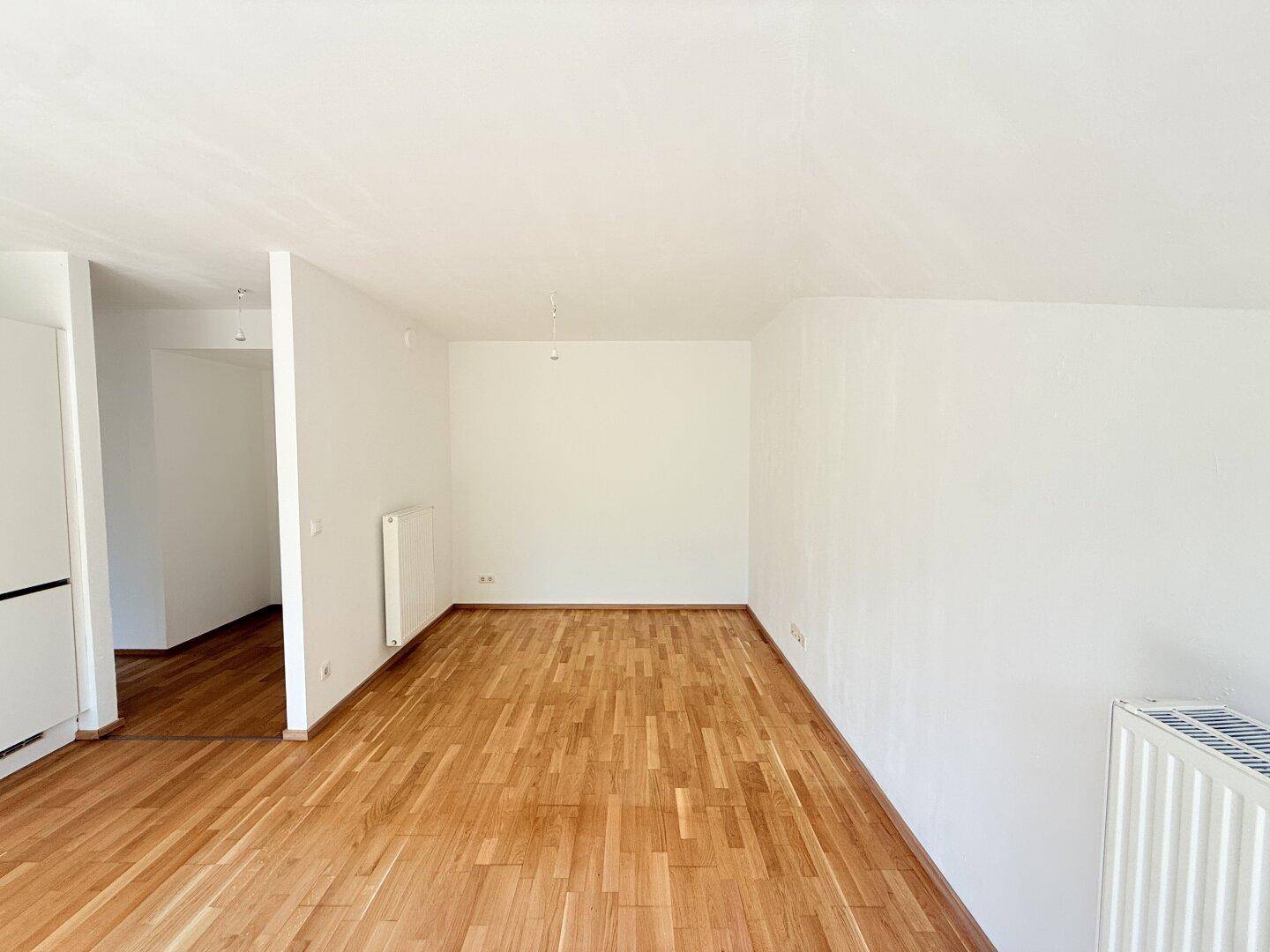 Geräumiger, heller Wohnbereich mit Holzparkett und weiß gestrichenen Wänden.